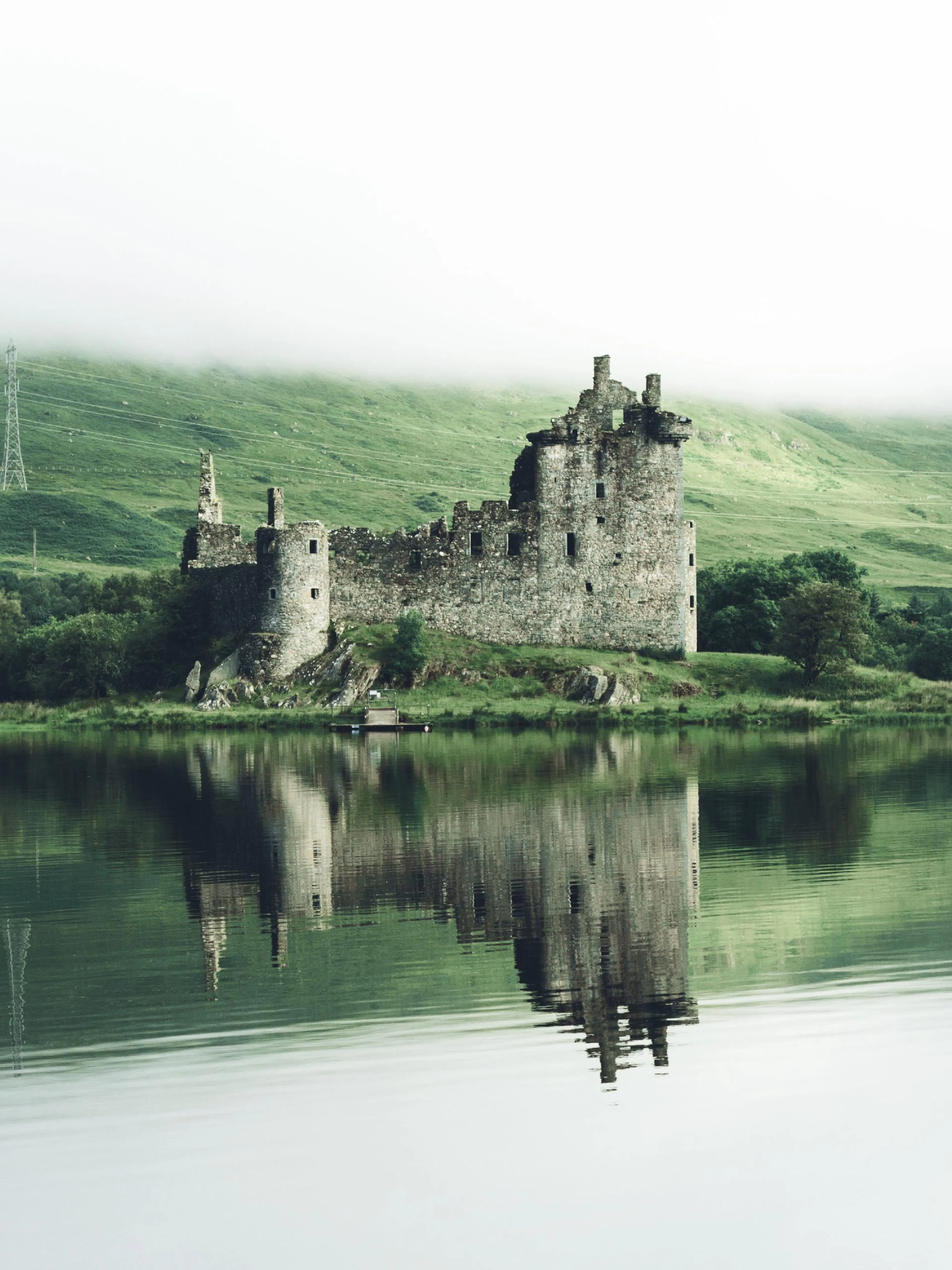 A poster featuring a historic Scottish castle ruin reflected in a calm, green lake under a misty sky.