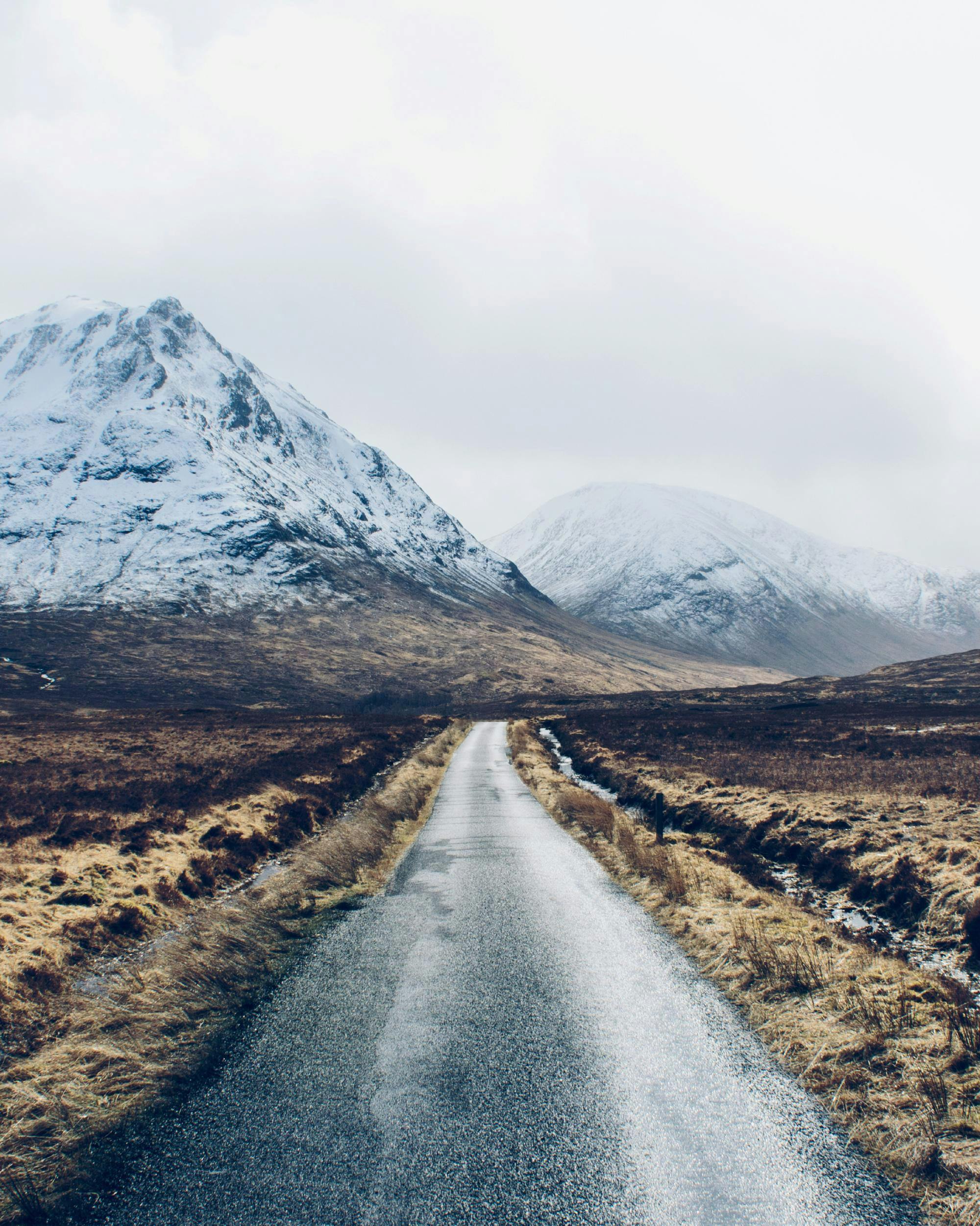 A poster featuring a straight road leading towards snow-capped mountains under a light sky in a barren landscape.