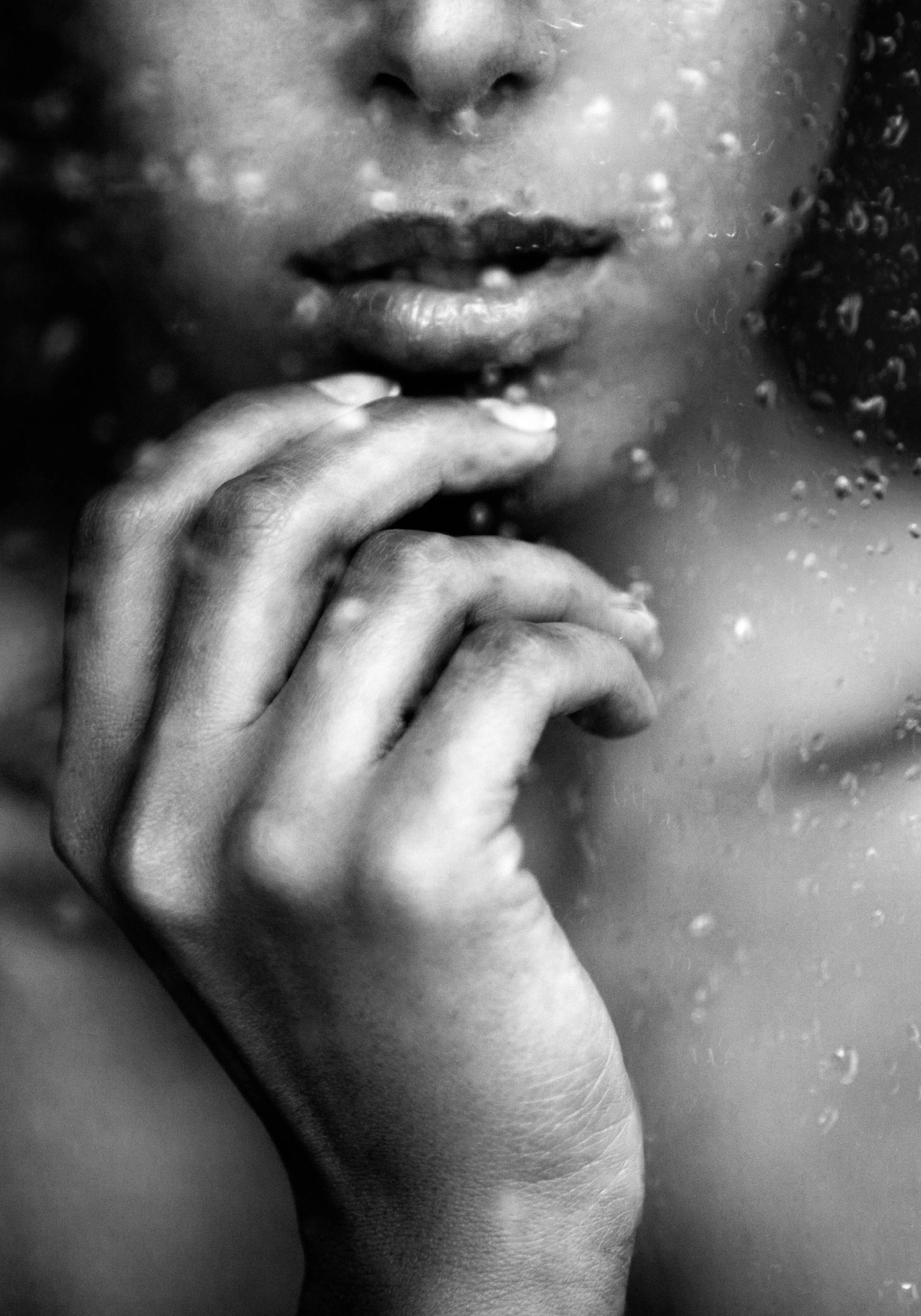 A black and white poster of a womans face and hand behind a wet glass, featuring her lips and fingers.