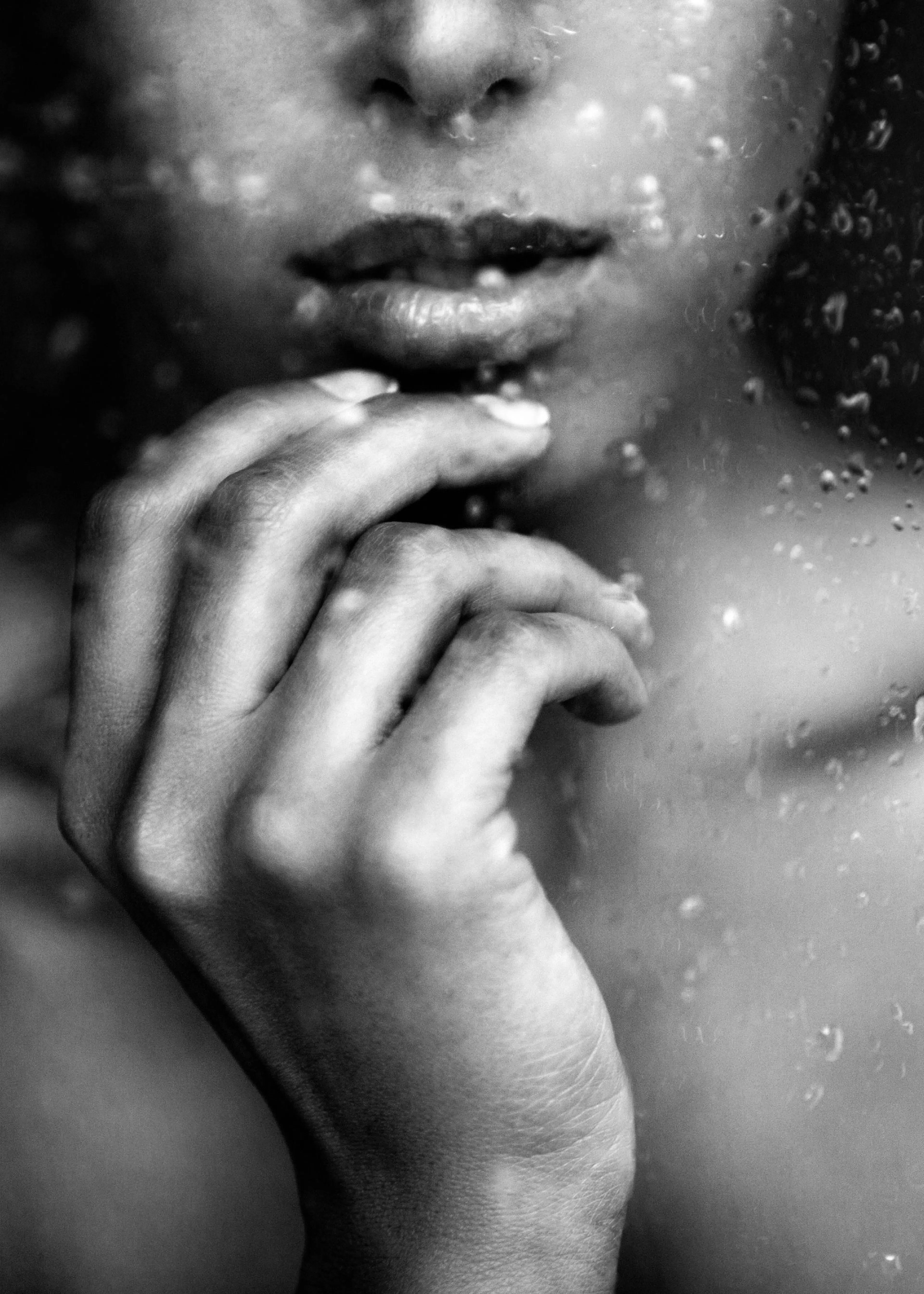 Mustavalkoinen juliste, jossa näkyy naisen kasvot ja käsi lasin läpi, jossa on sateen pisaroita.