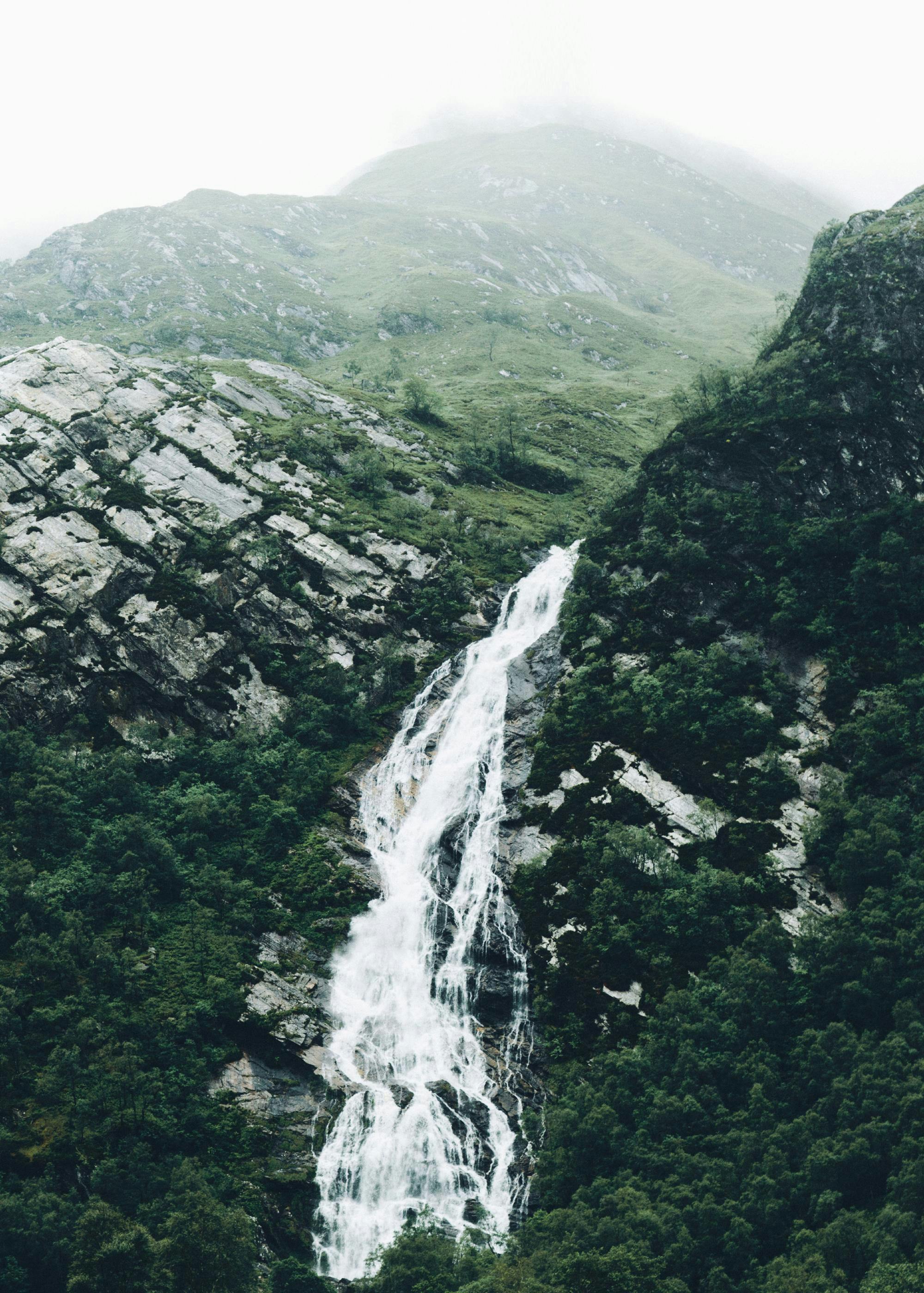 Ein Poster eines majestätischen Wasserfalls, der sich durch eine grüne Berglandschaft in Nebel hüllt.
