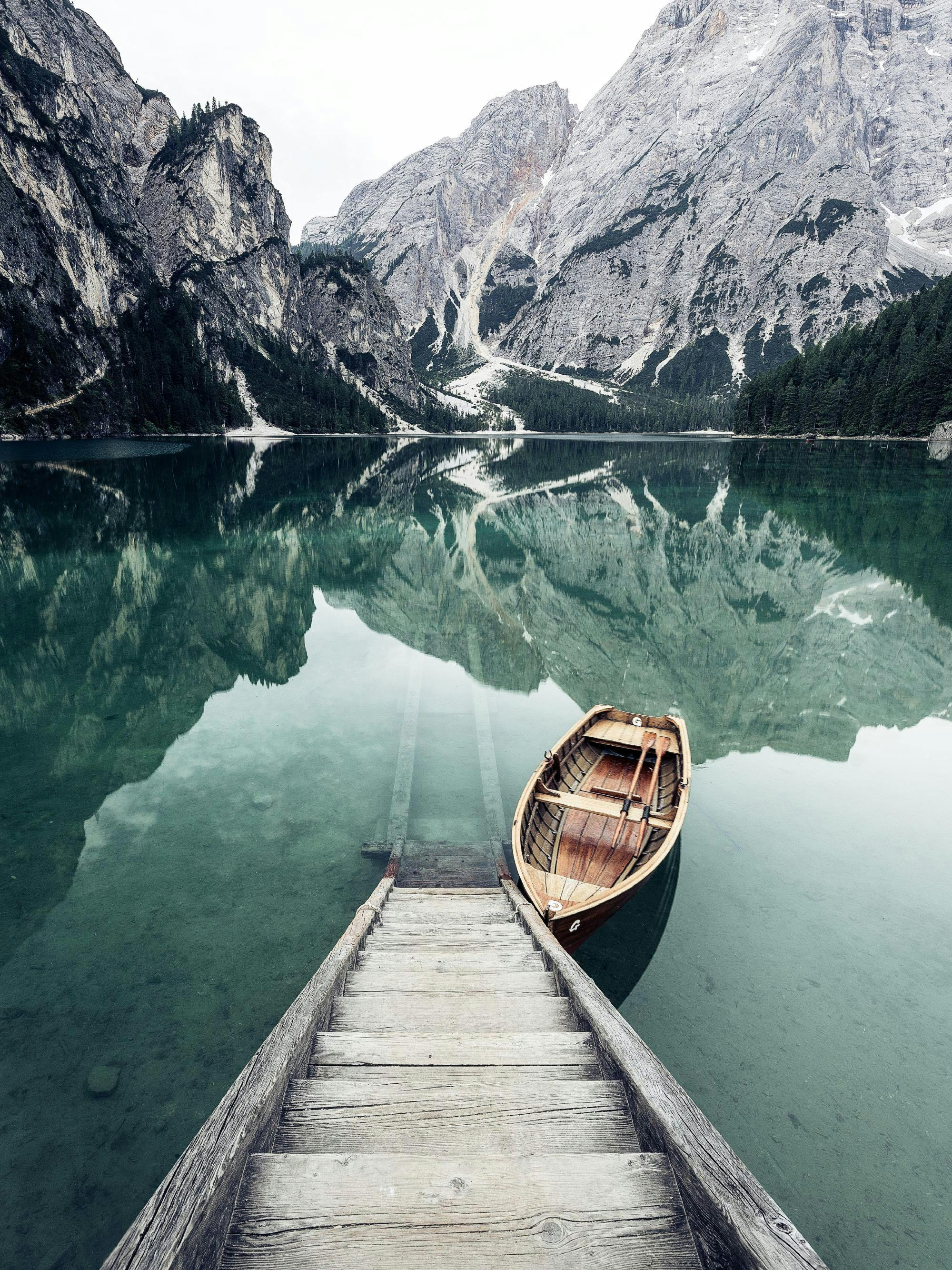 Een poster van een houten roeiboot aan een steiger in een bergmeer met weerspiegelende bergen.