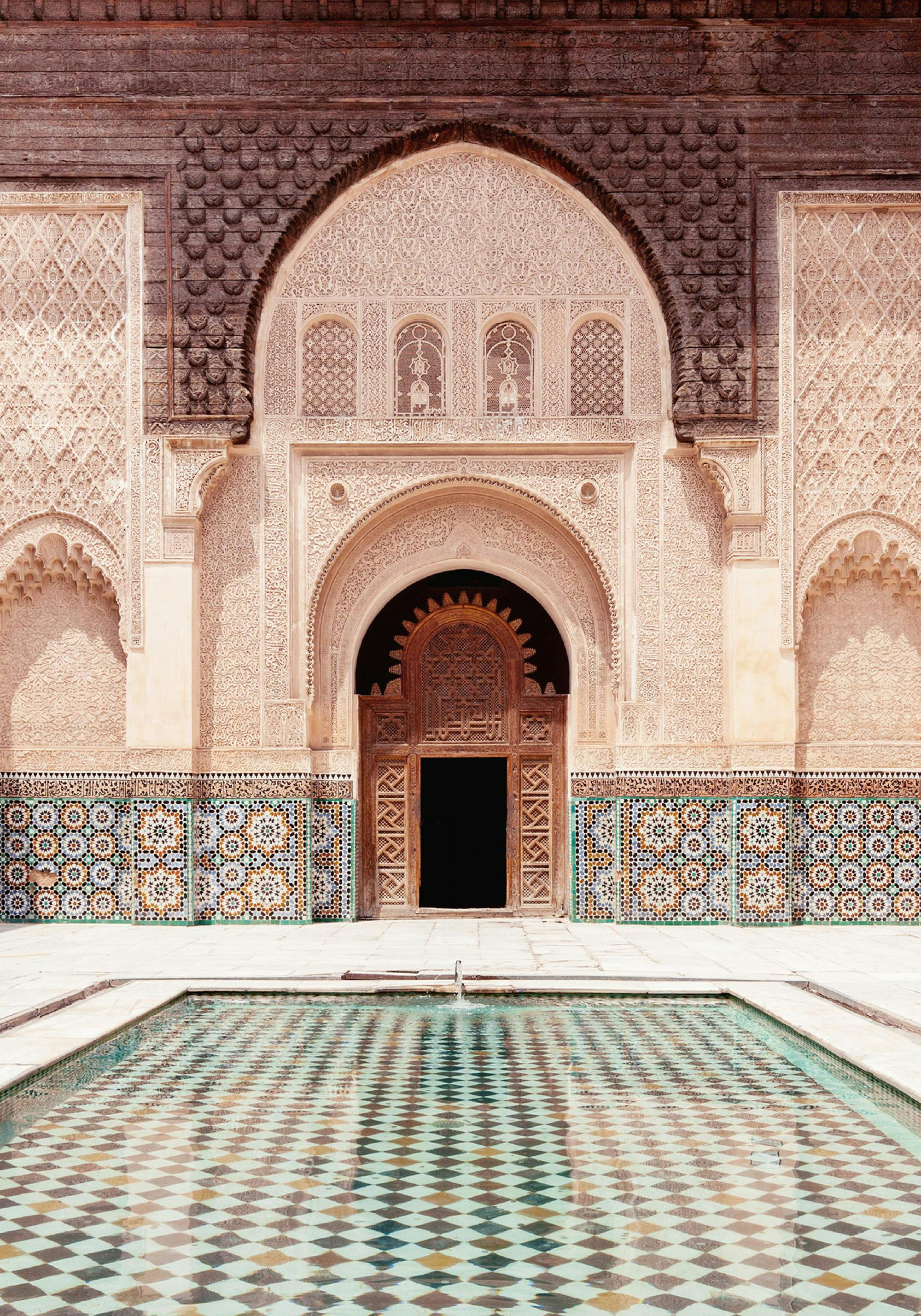 A poster featuring a Moroccan building with ornate carvings, mosaic tiles, and a reflecting pool with a checkered pattern.