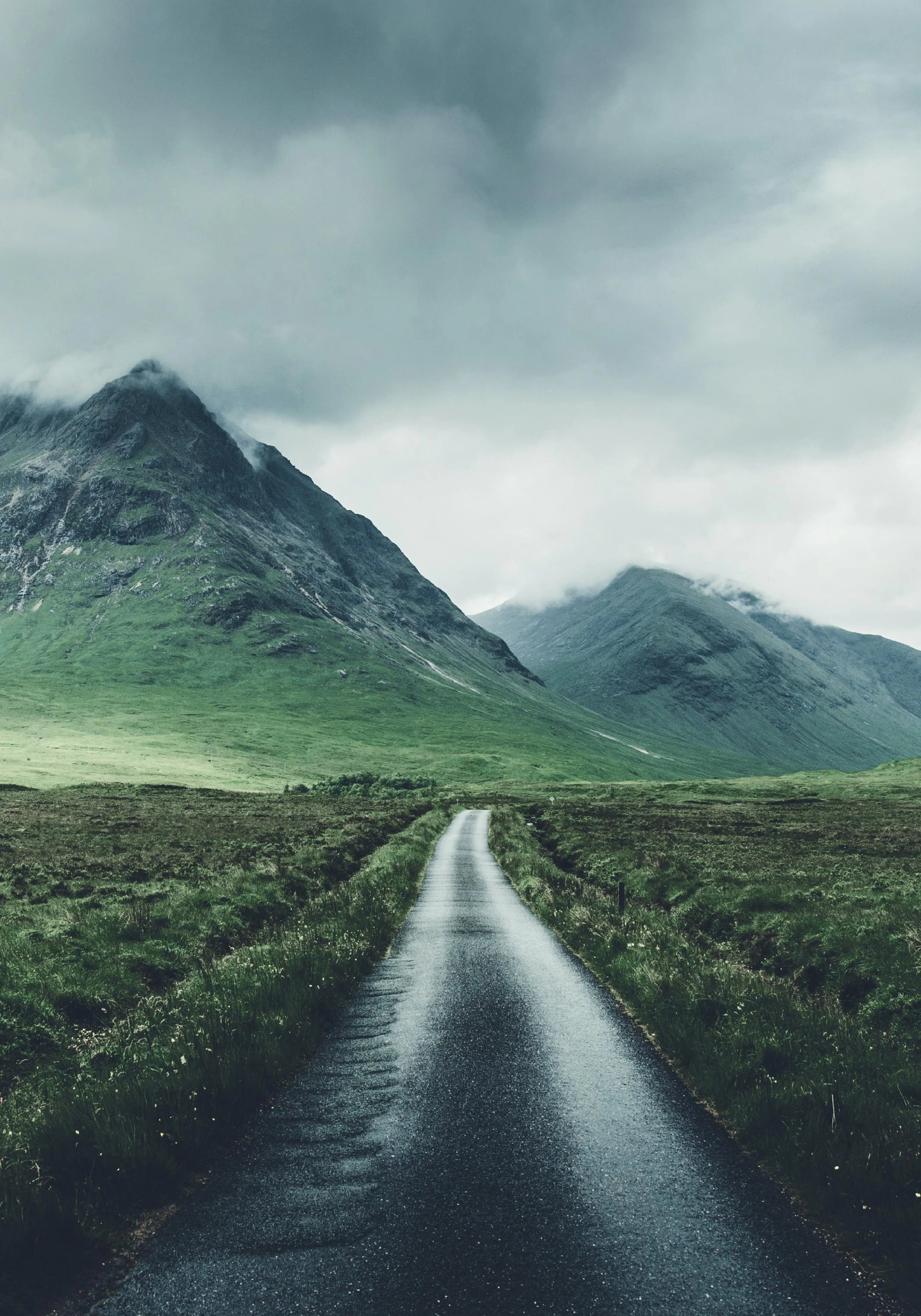 A poster featuring a moody landscape with a winding road through green hills and mountains under a cloudy sky.