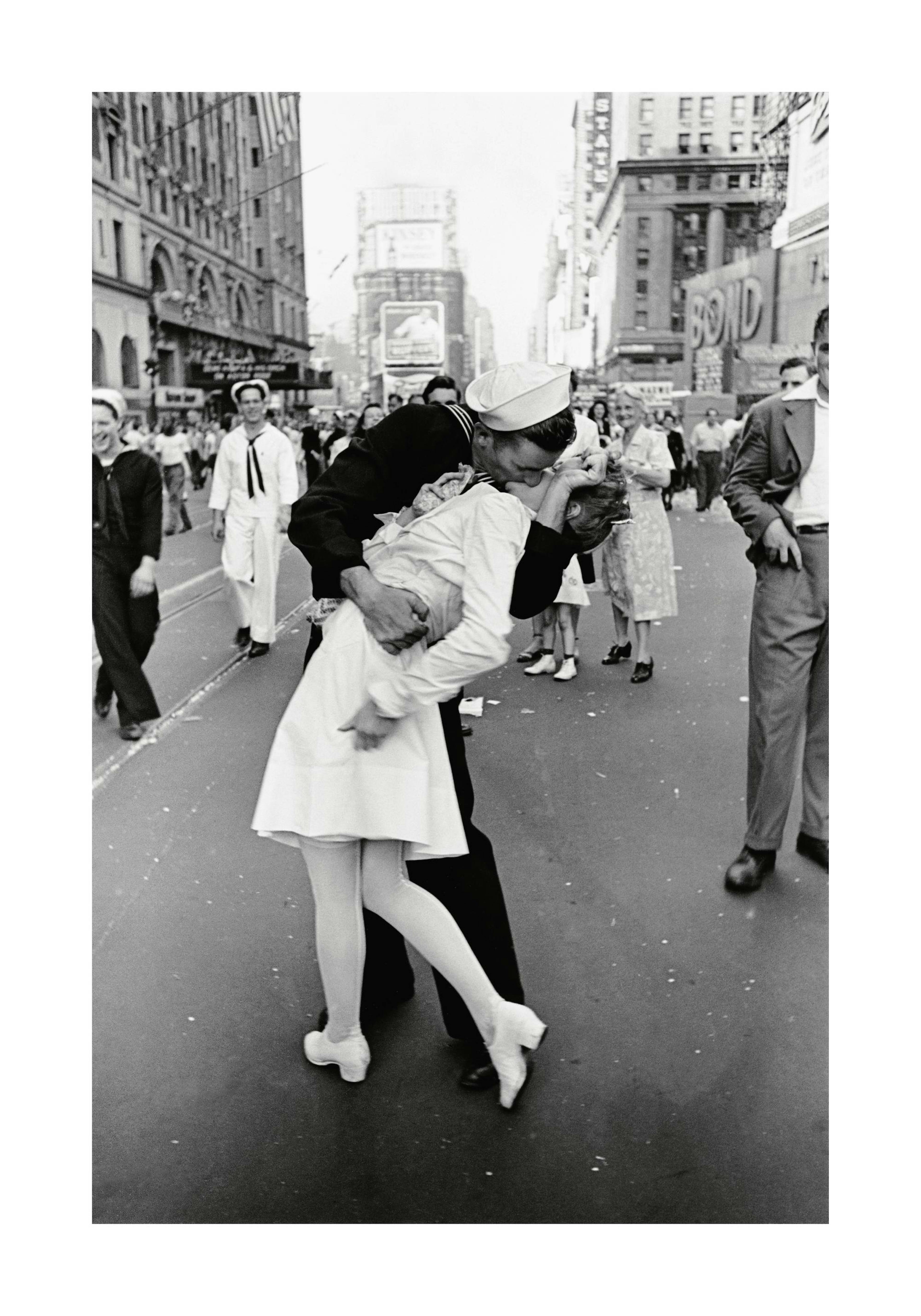 A black and white poster of a sailor kissing a nurse in a street, surrounded by cheering crowds and buildings.
