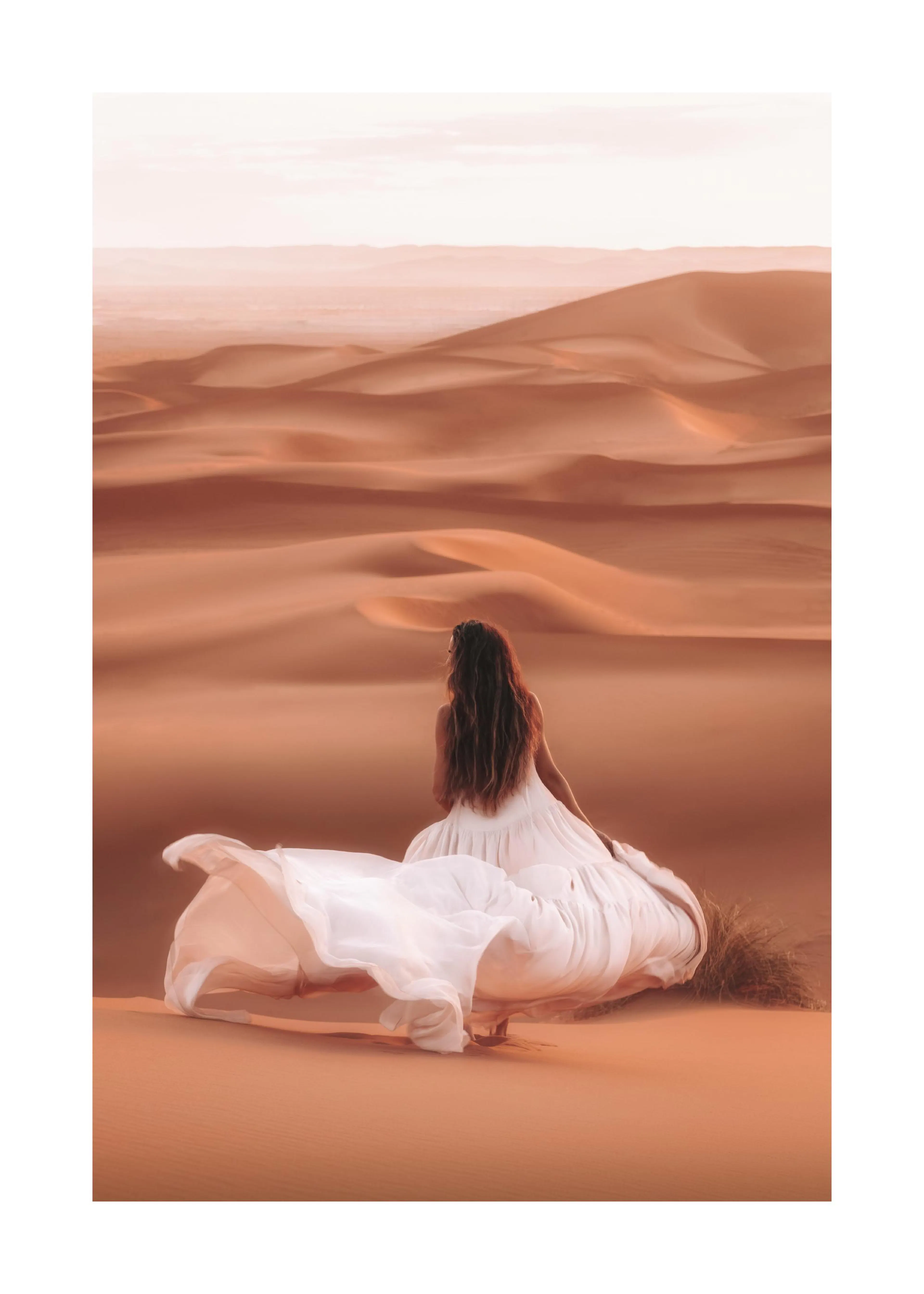 A poster featuring a woman in a flowing white dress sitting on a sandy dune, looking out over a vast desert landscape.