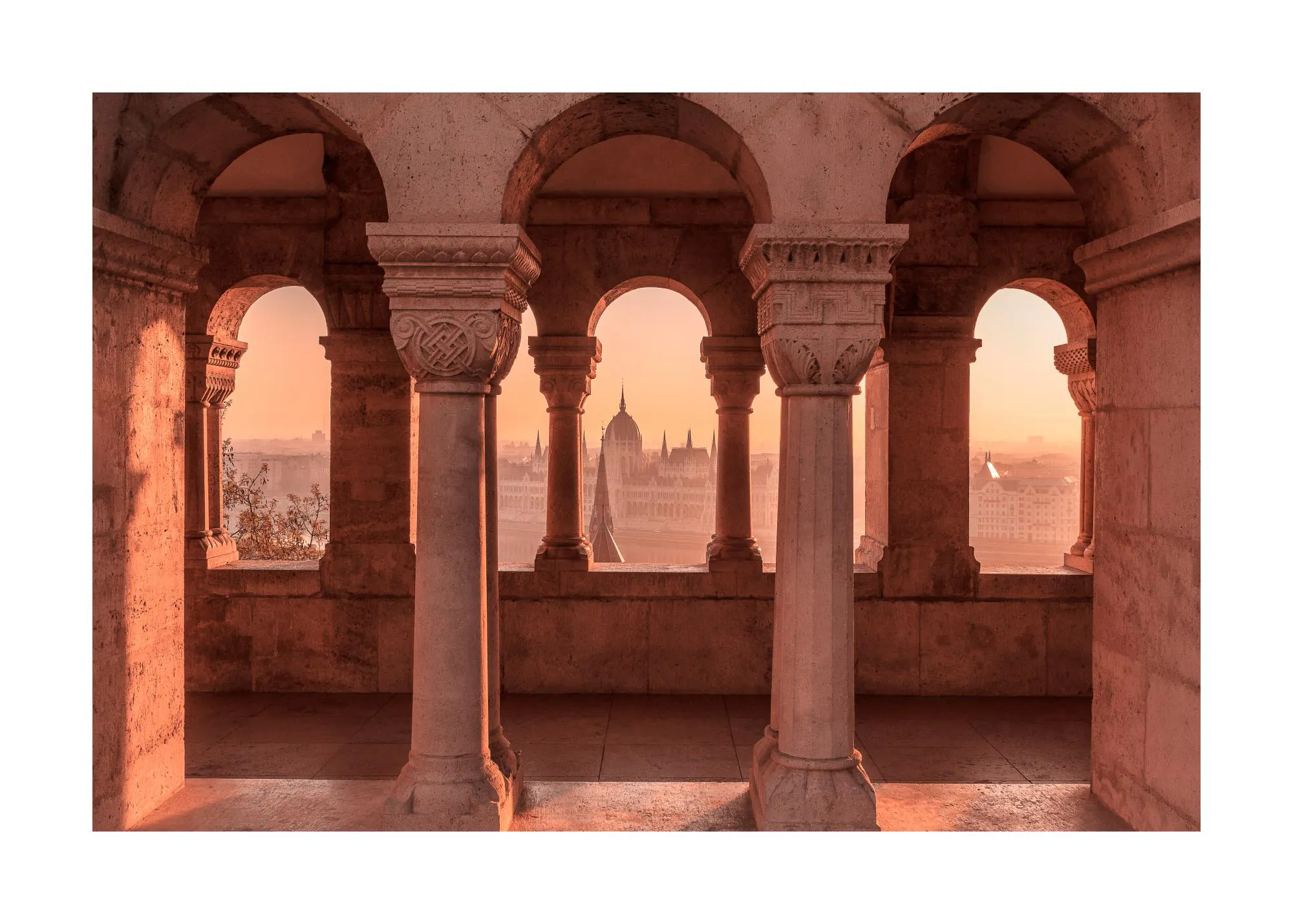 A poster depicting a view through ornate stone arches and columns, revealing the Hungarian Parliament Building at sunset.