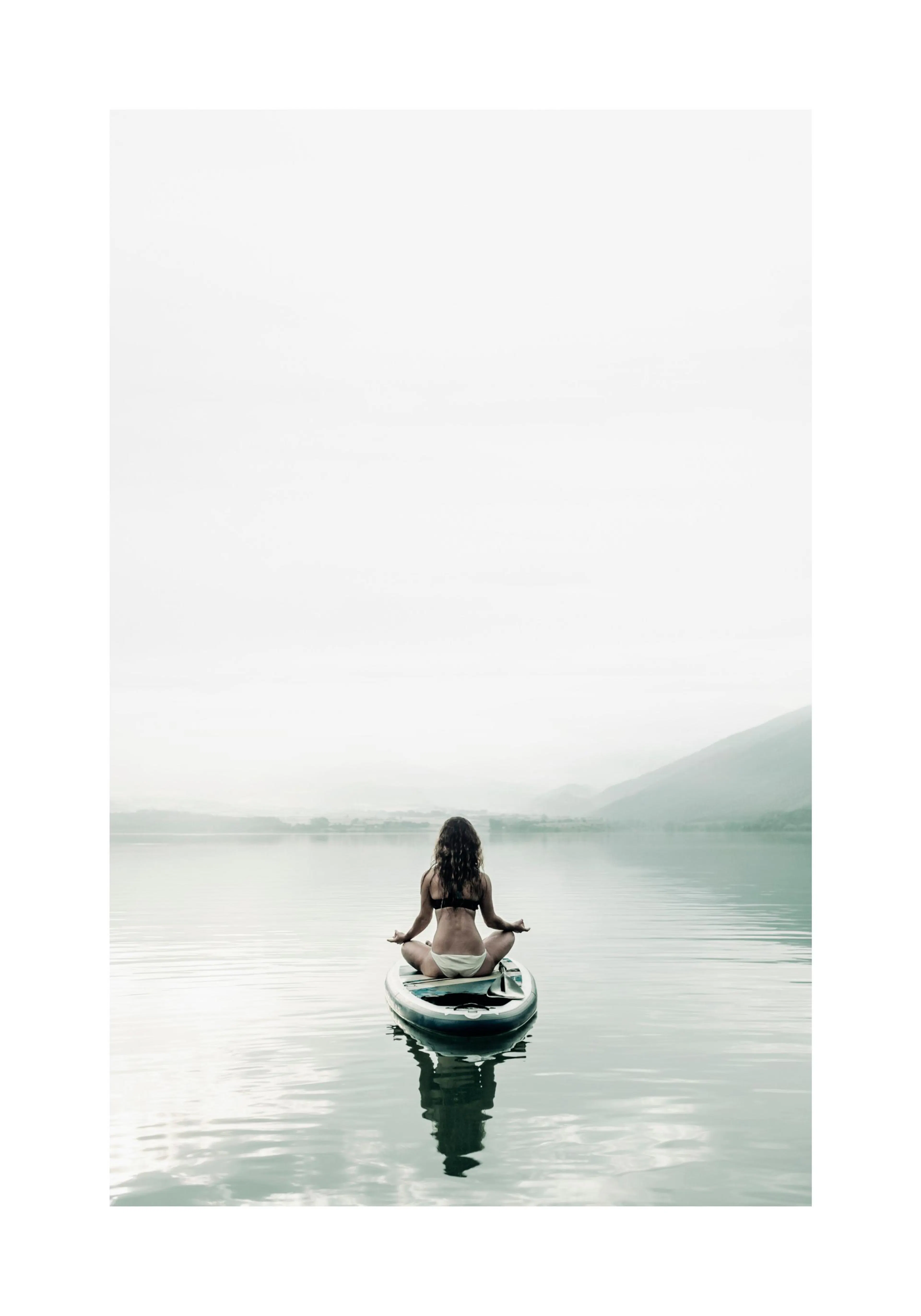A poster featuring a woman meditating on a paddleboard in the middle of a calm lake with mountains in the background.