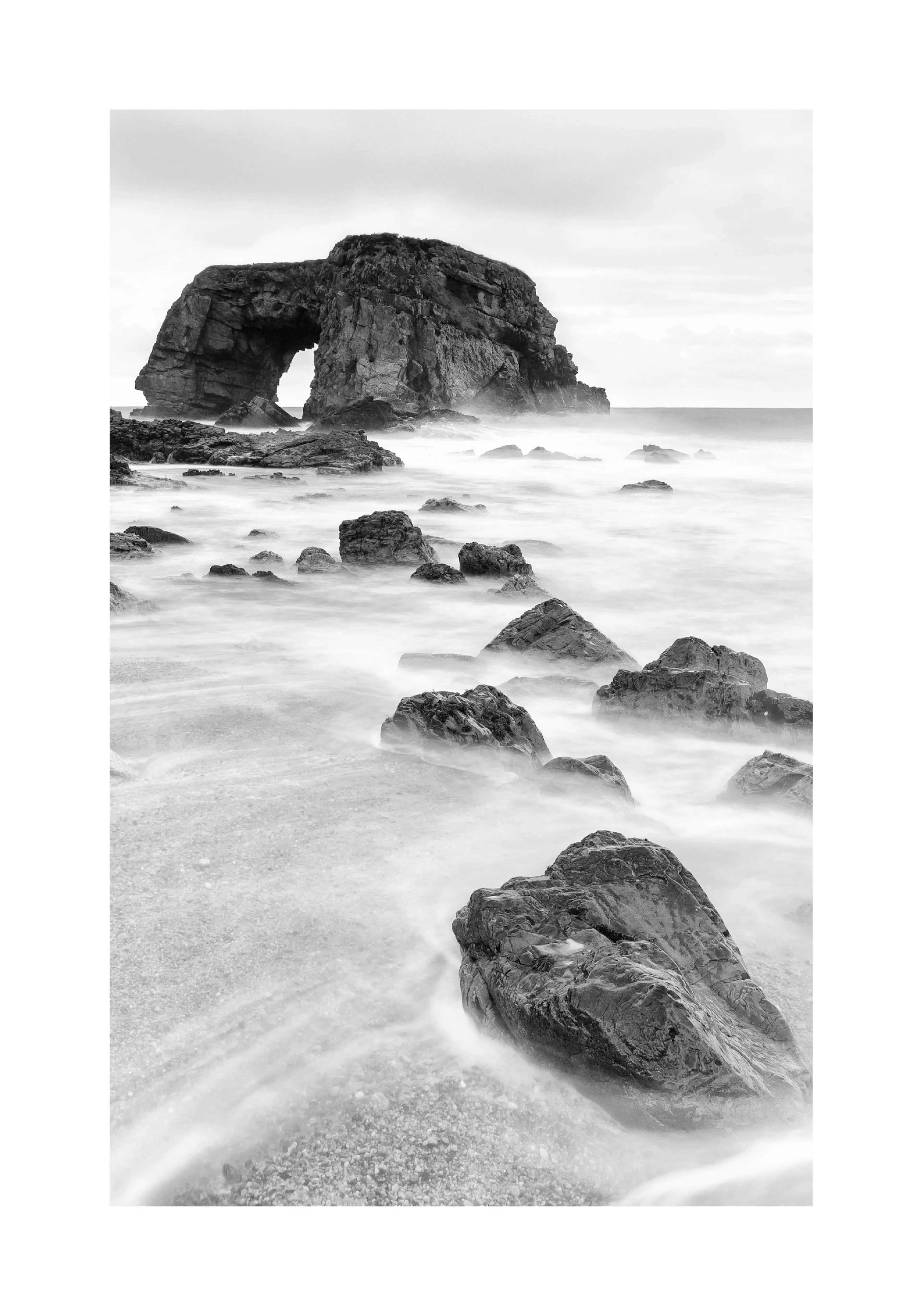 A black and white poster of a natural rock arch formation with blurred water flowing around rocks on a beach.