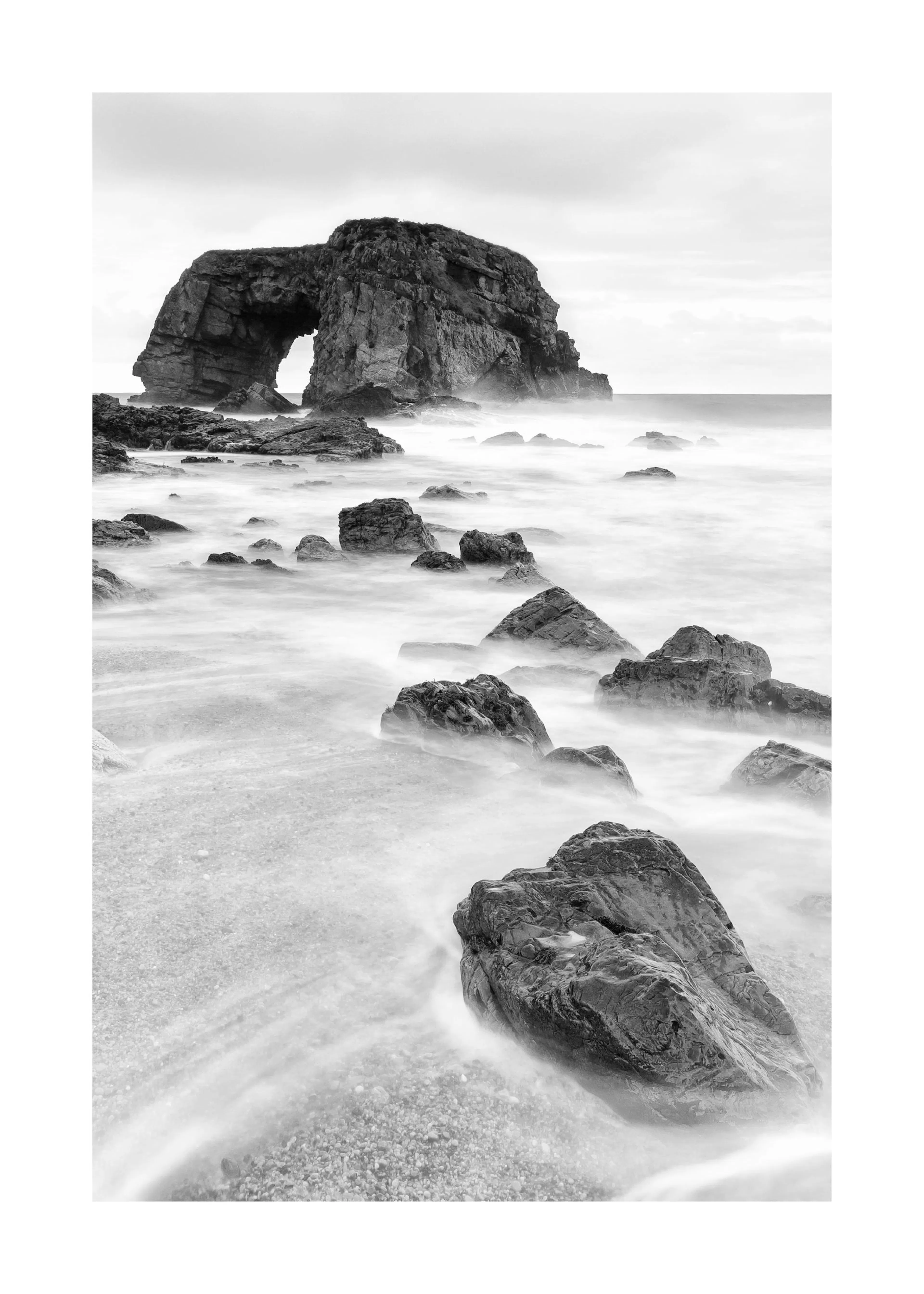 A black and white poster of a rocky sea arch over misty water, with smooth rocks in the foreground.