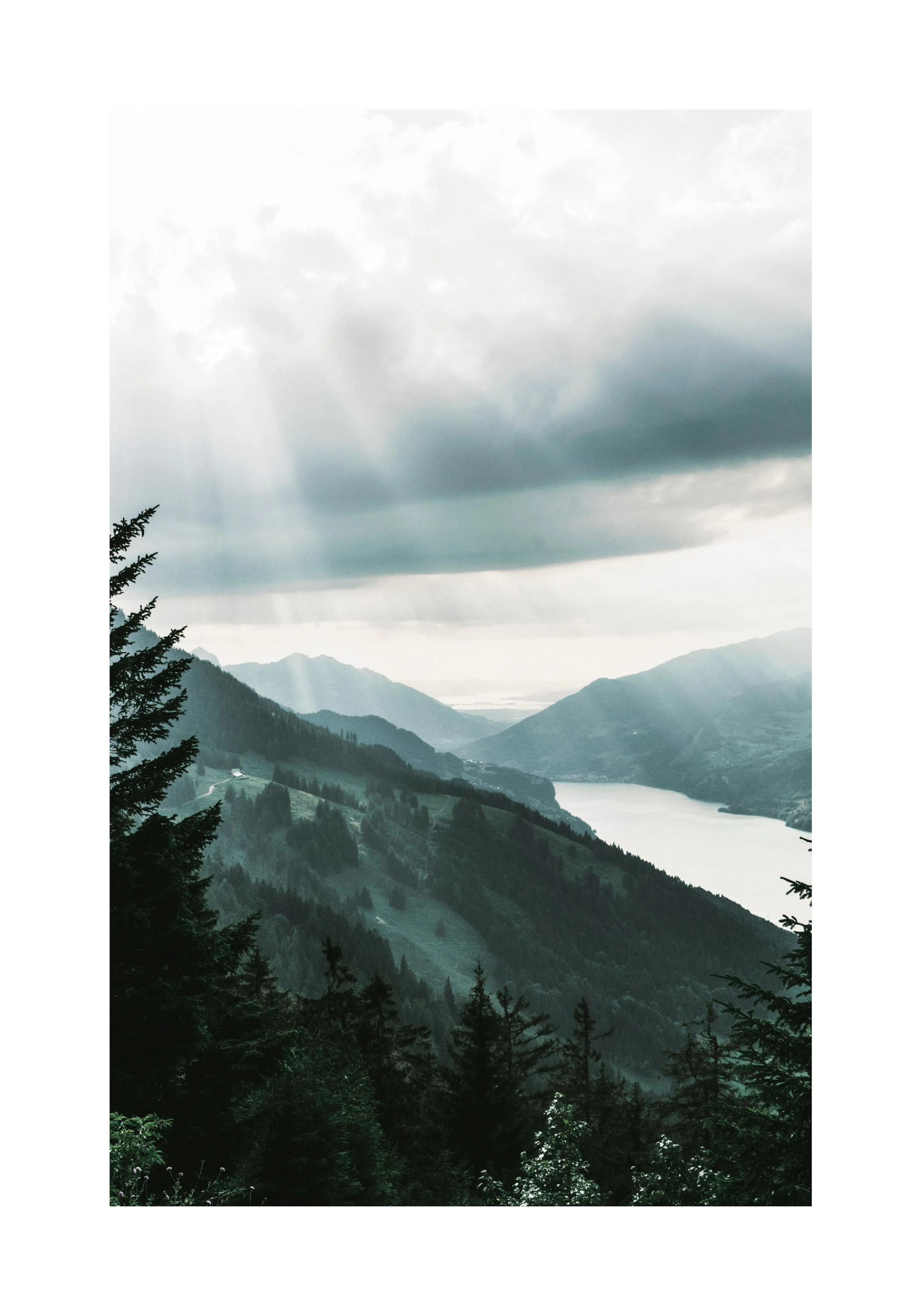 A poster featuring a mountain landscape with sunrays breaking through clouds over a lake and dark green forests.