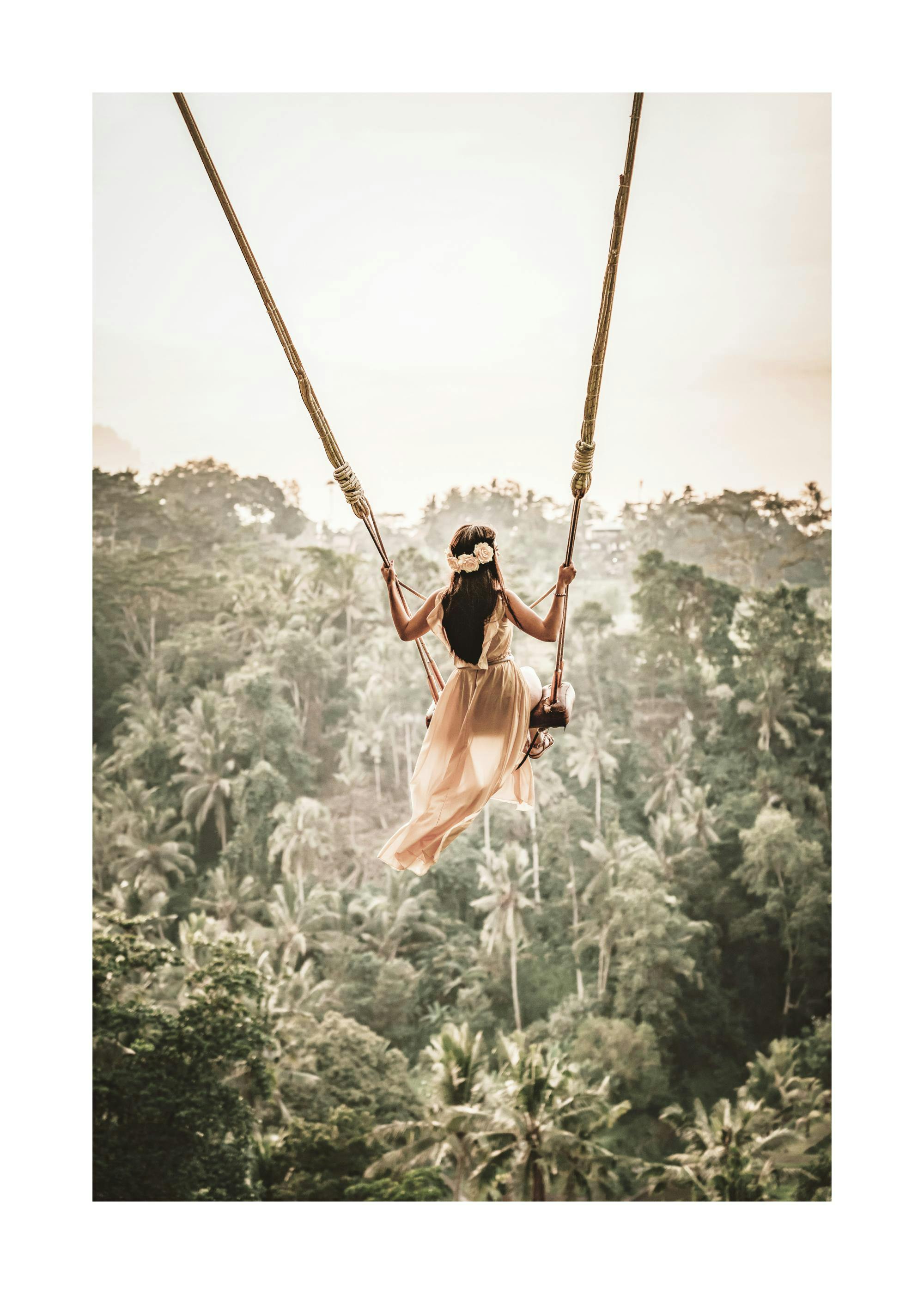 A poster featuring a woman in a long flowing dress on a swing overlooking a lush tropical jungle landscape.