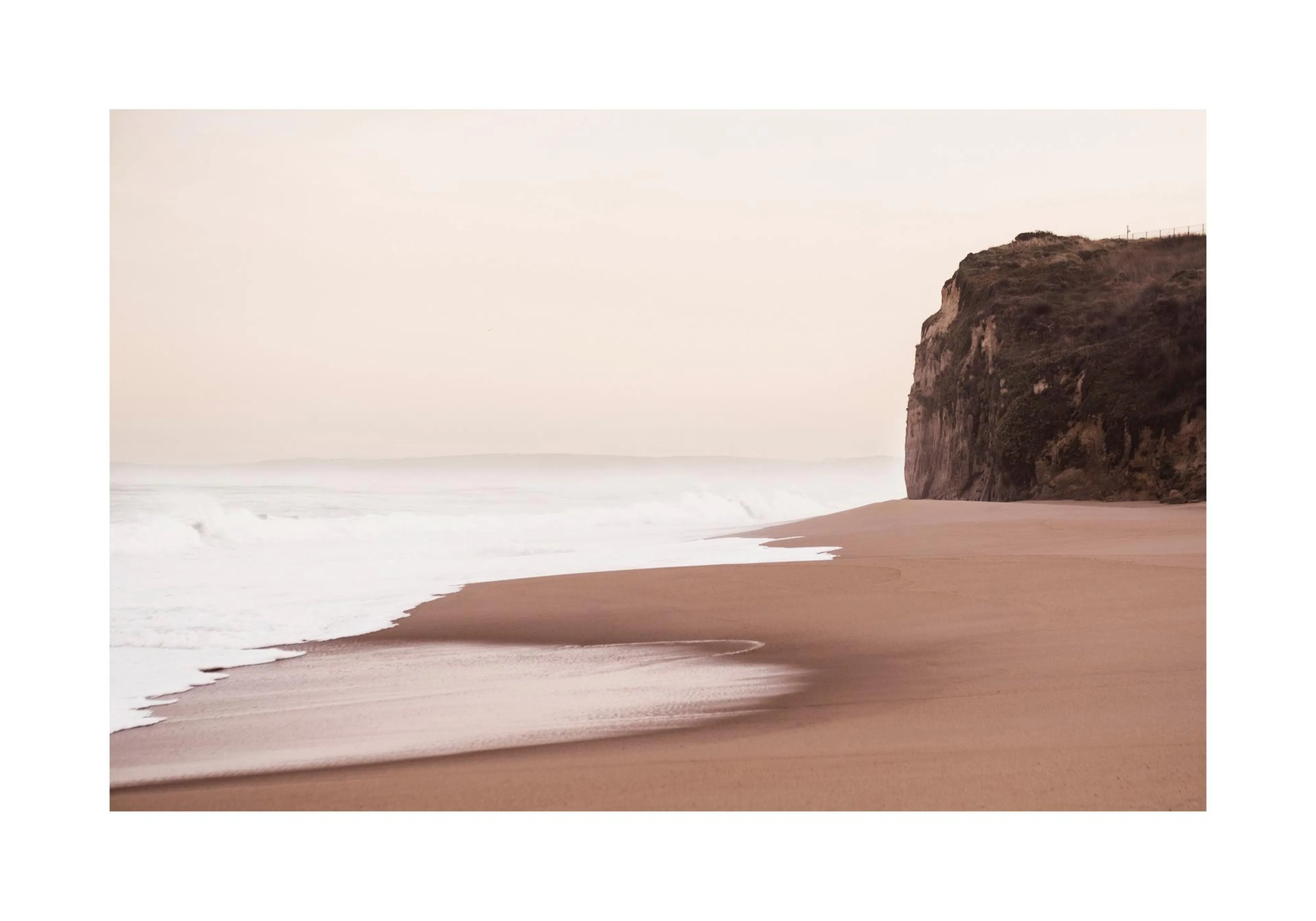A poster featuring a tranquil beach scene with white foamy waves receding on a sandy shore next to a large cliff under a light s