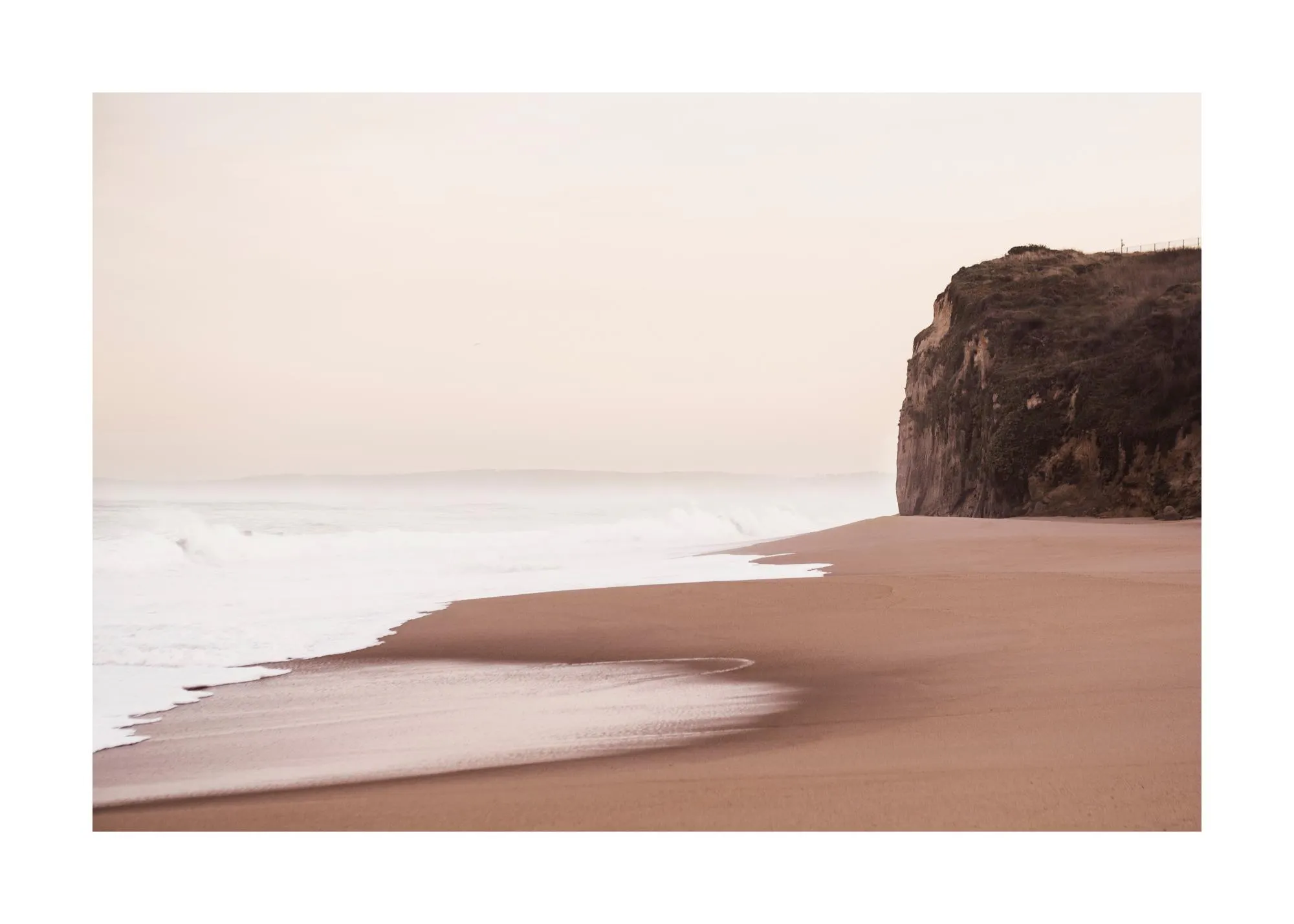 Un poster di una spiaggia con sabbia color terracotta e onde bianche che si infrangono, sotto una scogliera rocciosa.