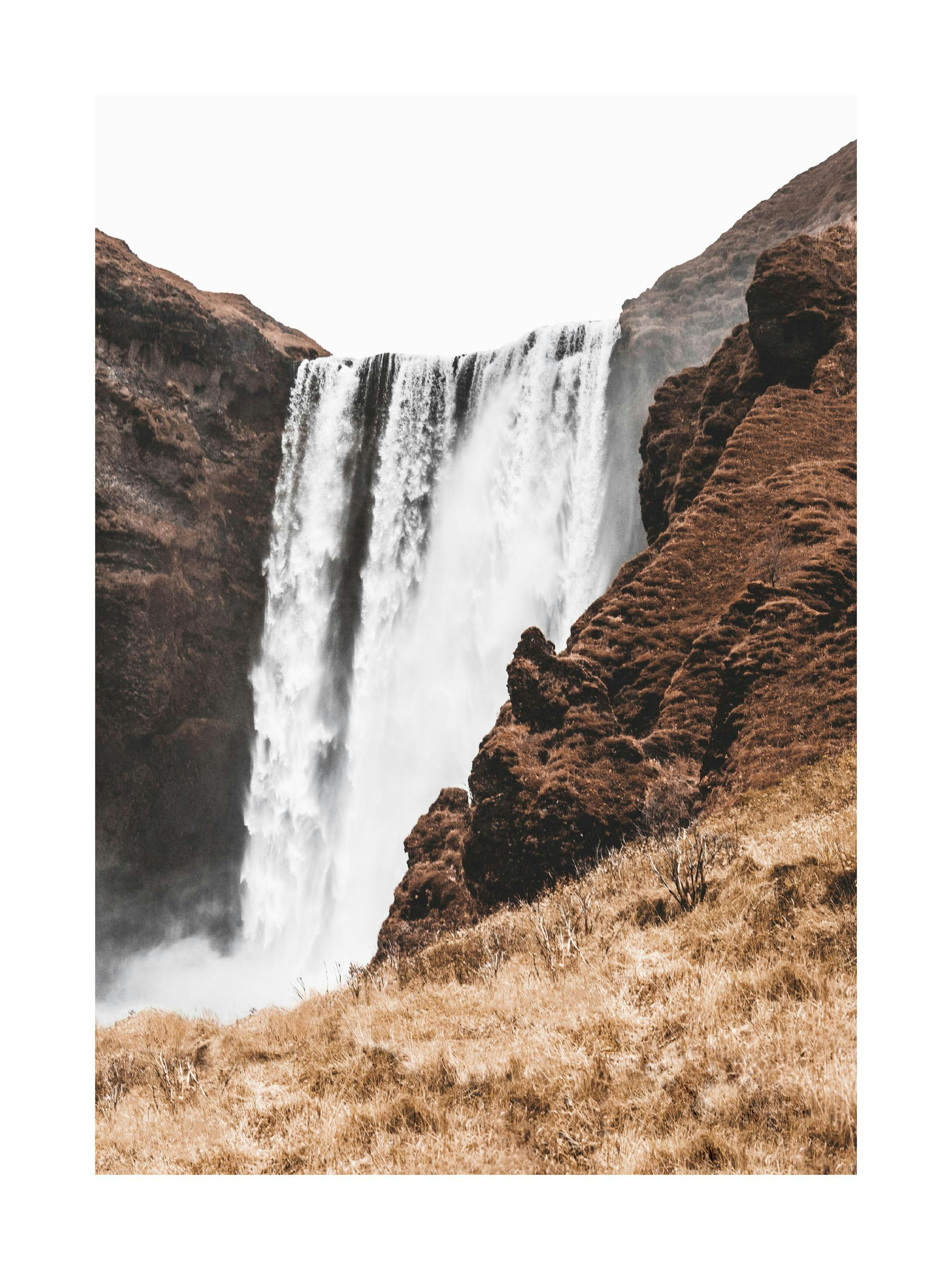 Poster con cascata maestosa che scende tra rocce marroni e vegetazione giallastra sotto un cielo chiaro.
