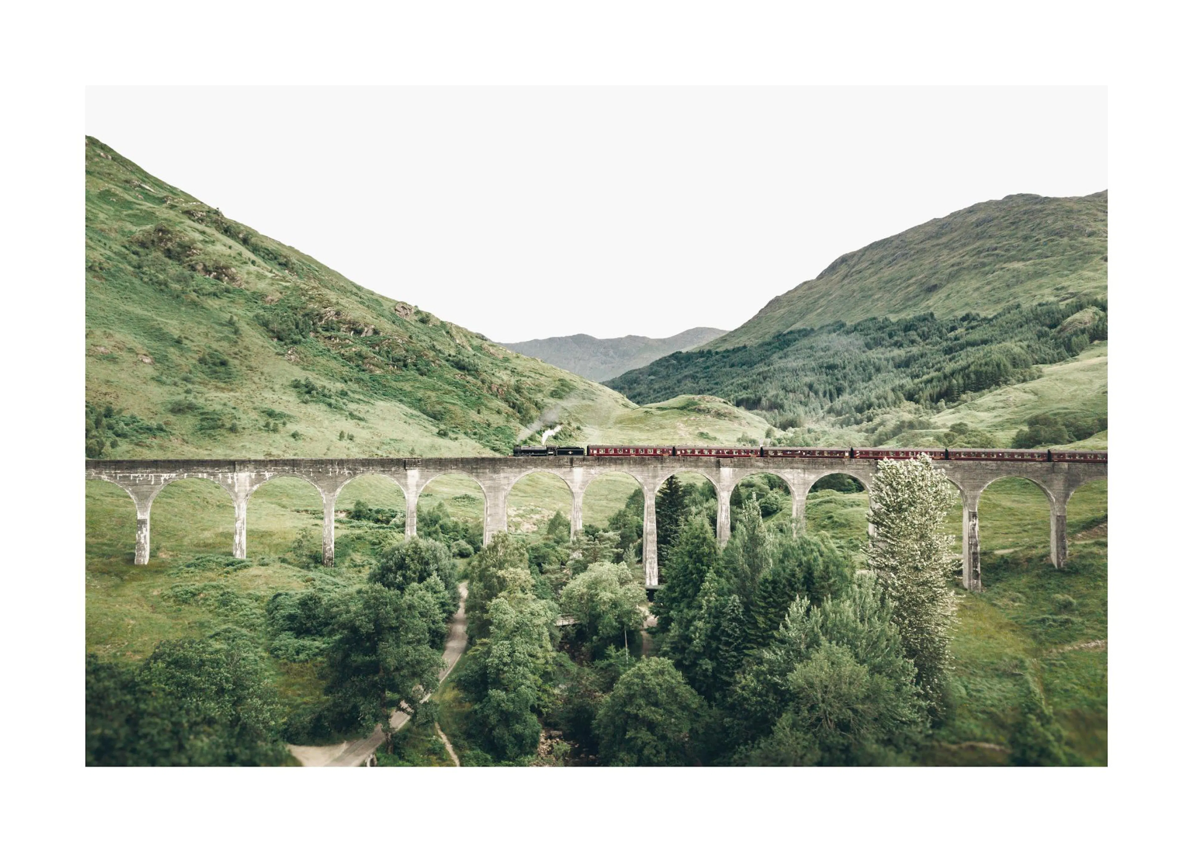 Poster: Ein Zug fährt über ein Viadukt in einer grünen Berglandschaft mit Bäumen und einem hellen Himmel.