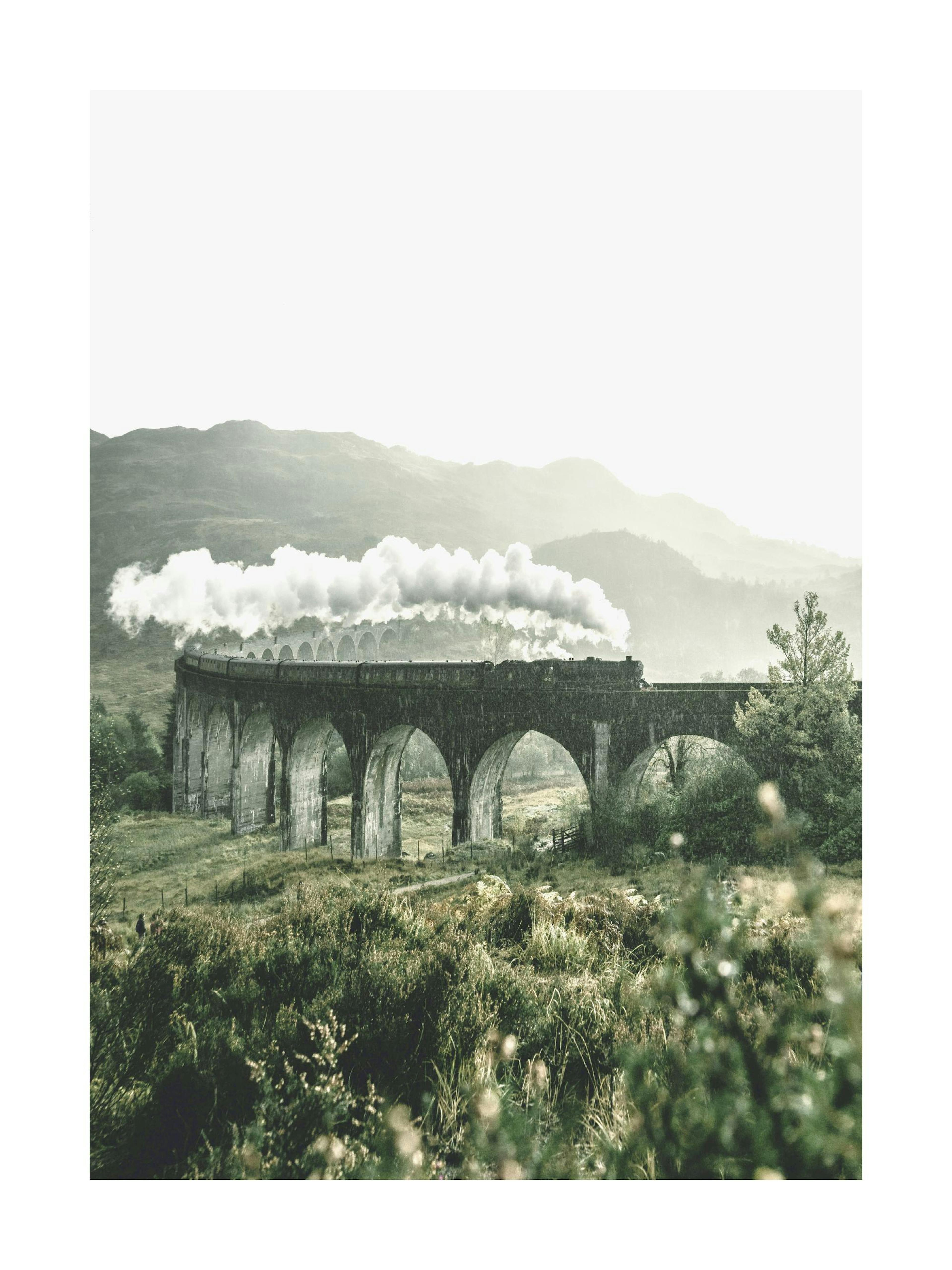 A poster depicting a steam train on a viaduct, with white smoke billowing, against a misty mountain backdrop.