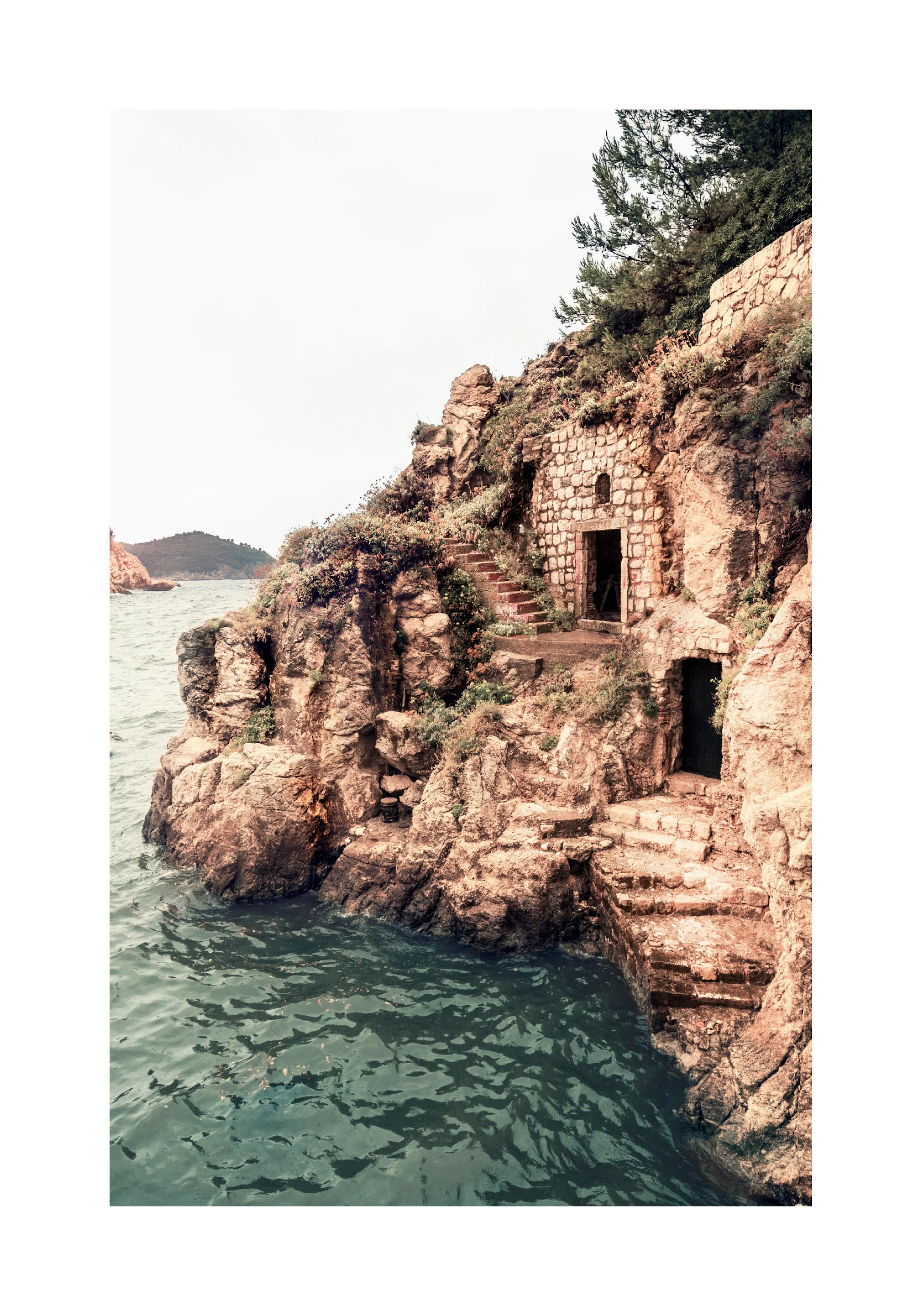 A poster featuring a stone building and steps built into a rocky cliff face, with the ocean at its base.