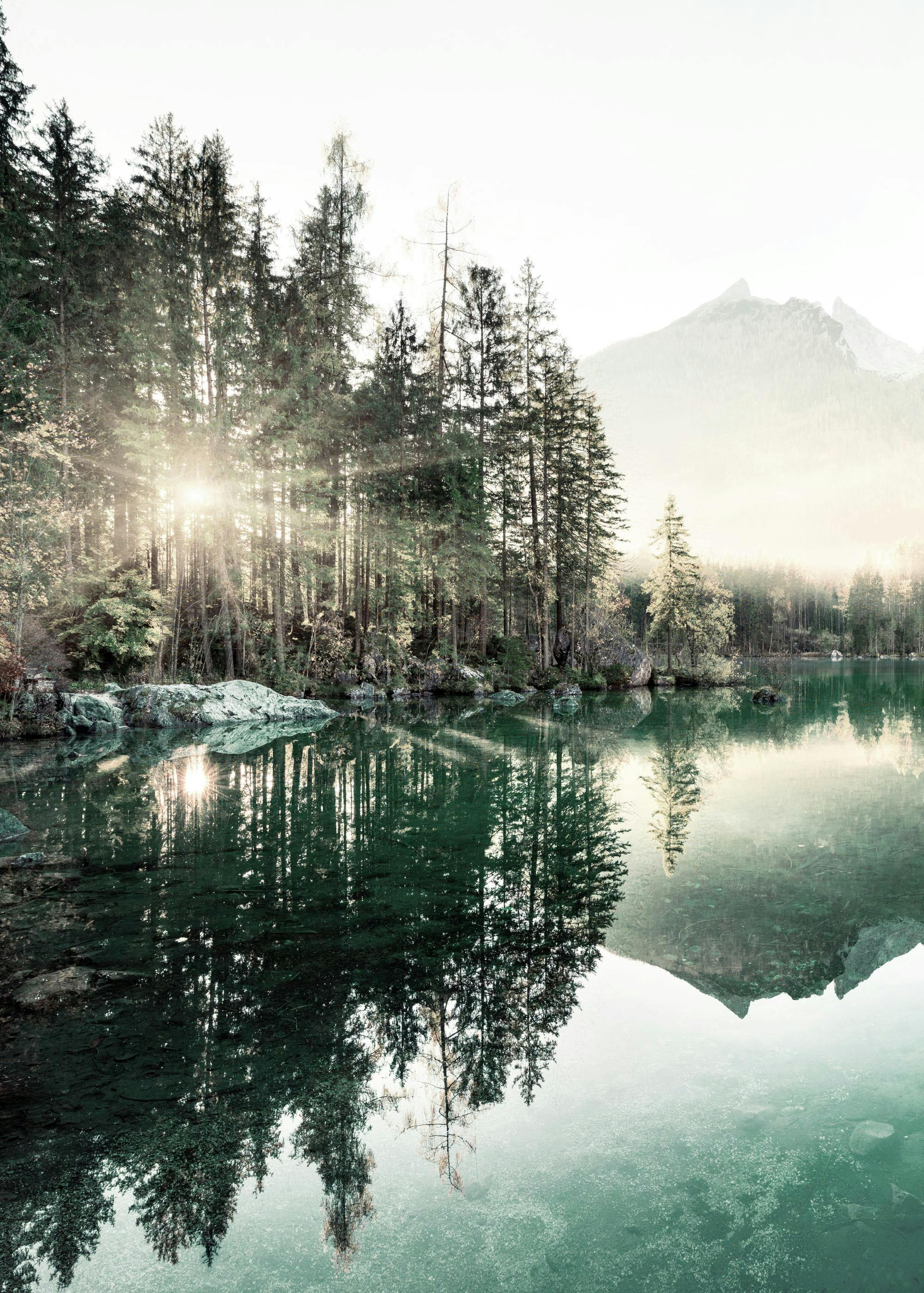 Poster dun lac turquoise reflétant une forêt de conifères et une montagne brumeuse sous un soleil éclatant.