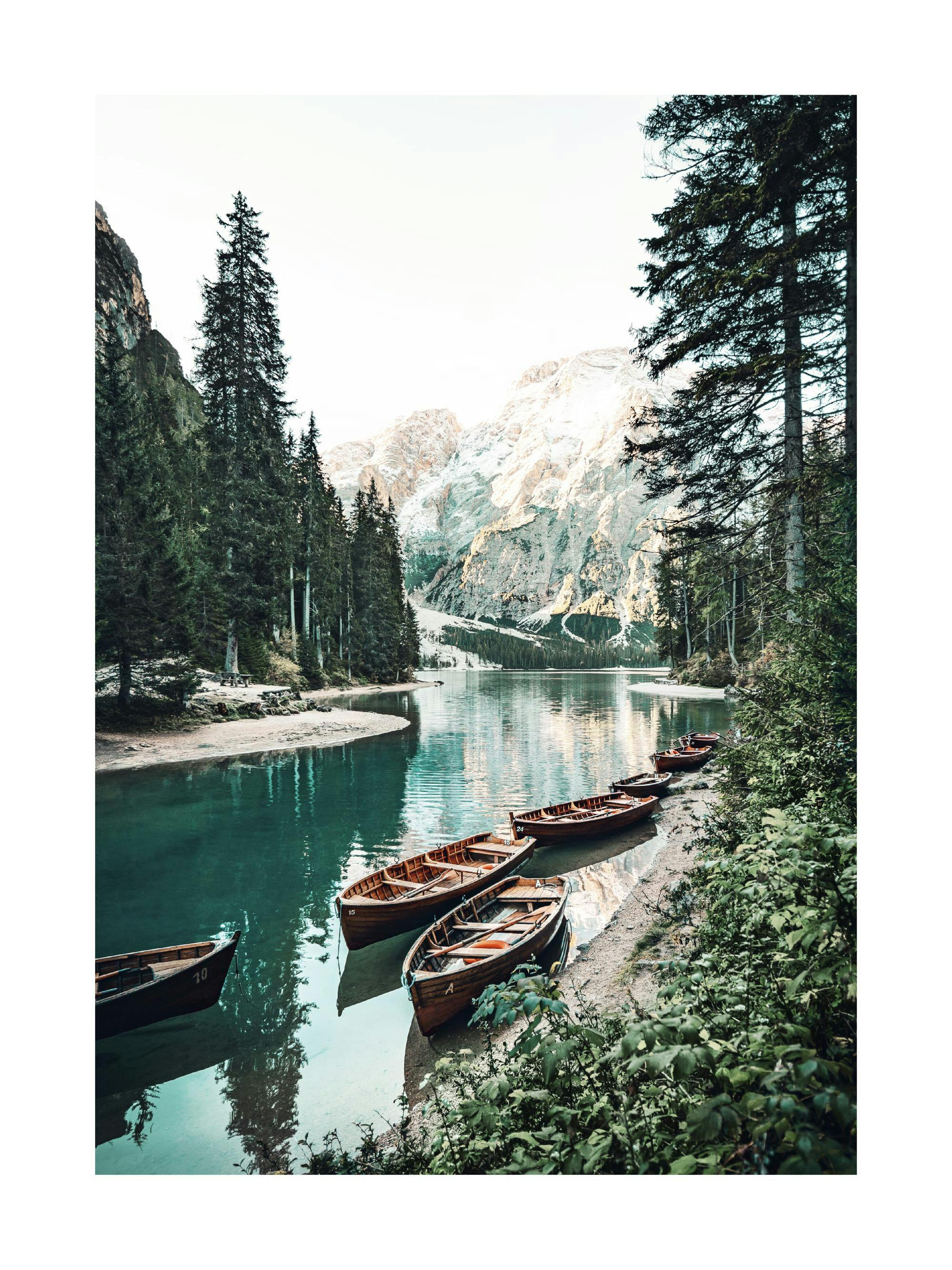 Poster dun lac turquoise avec des bateaux en bois amarrés et des montagnes enneigées en arrière-plan.