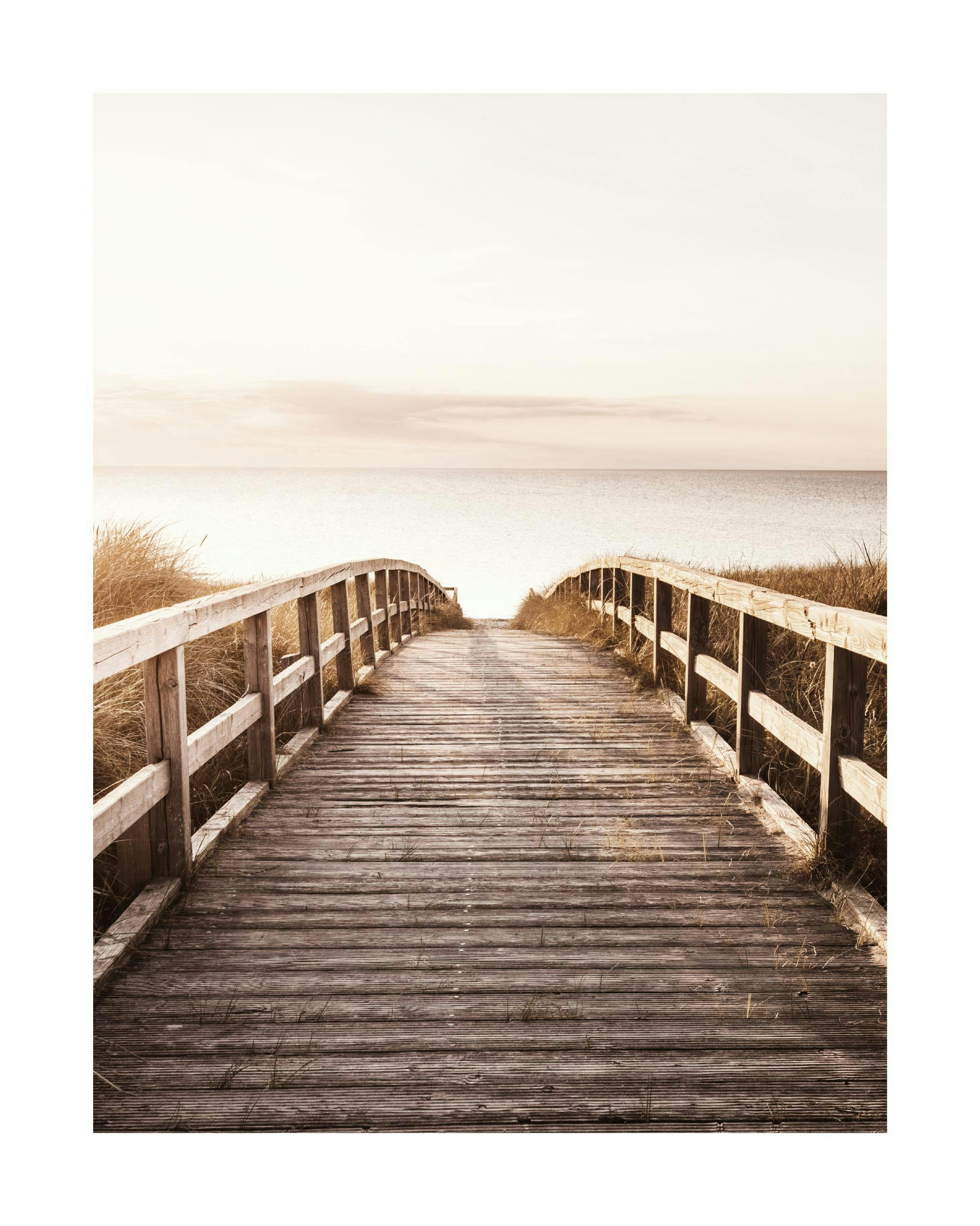 A poster featuring a wooden boardwalk over sand dunes leading to a calm sea under a soft, clear sky.