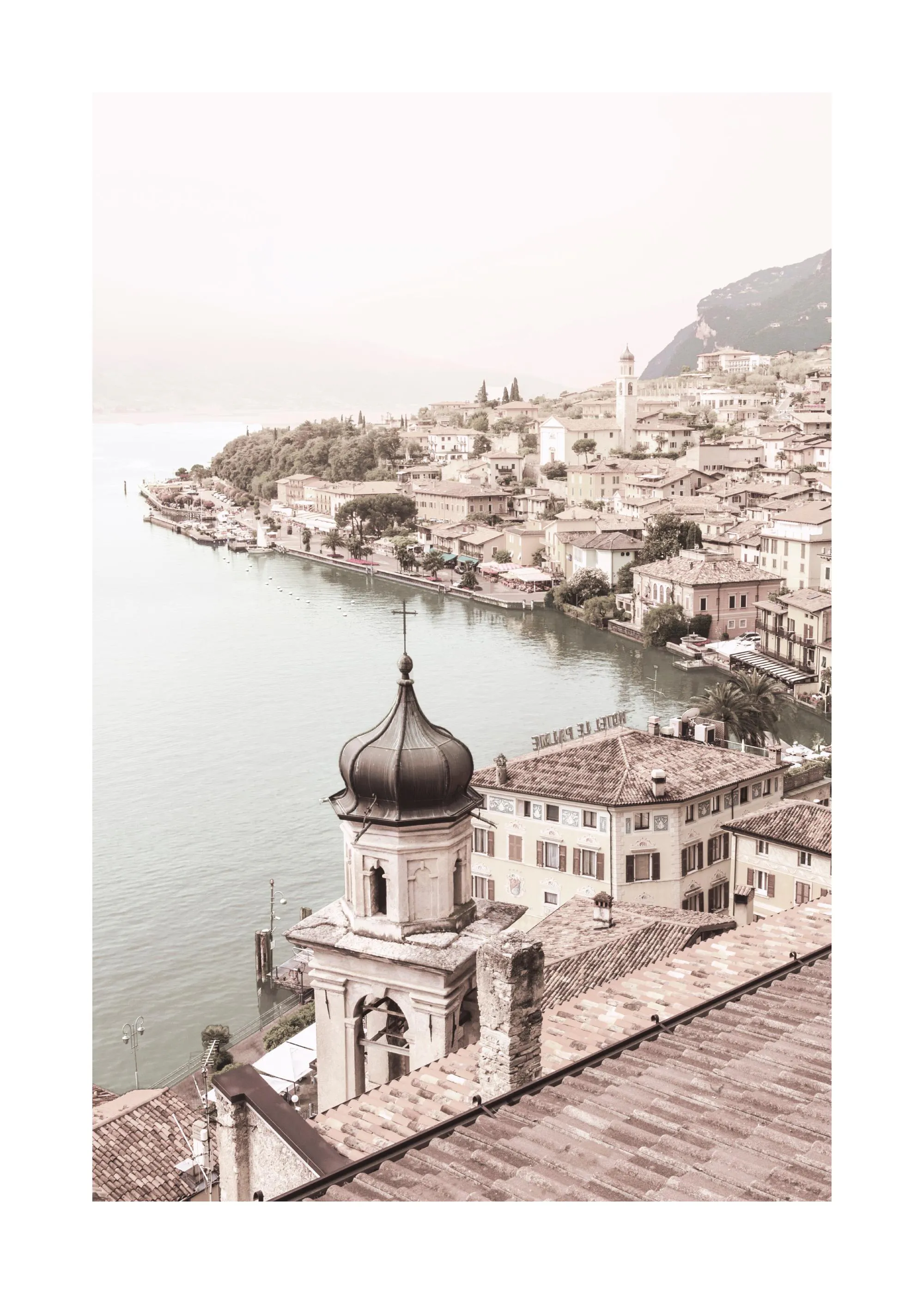 En poster som visar en lugn italiensk by vid en sjö, med tegelröda hustak och en kyrka med kupol.
