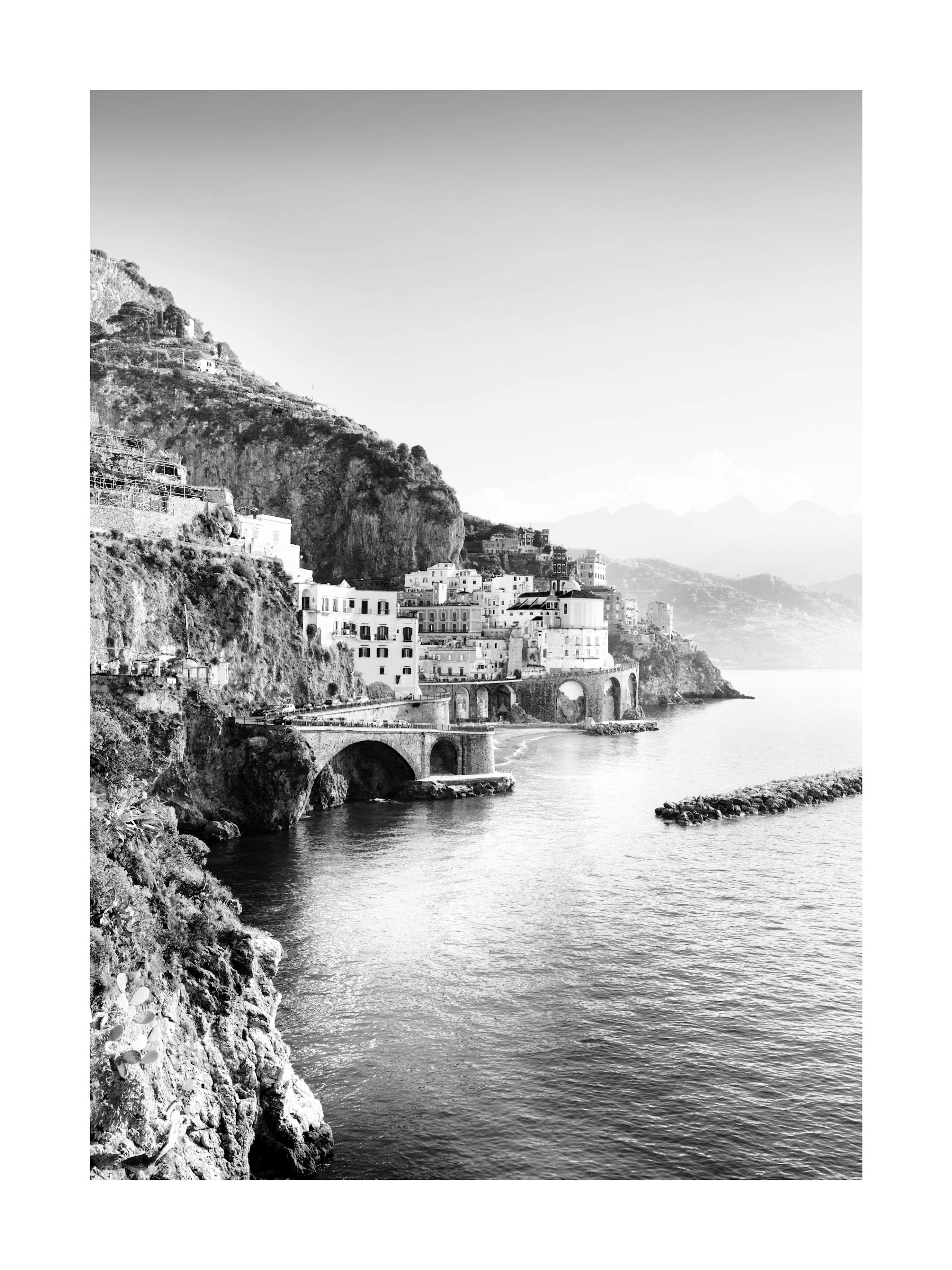 A black and white poster featuring a coastal town built into a high cliff face, with arched bridges over the water.