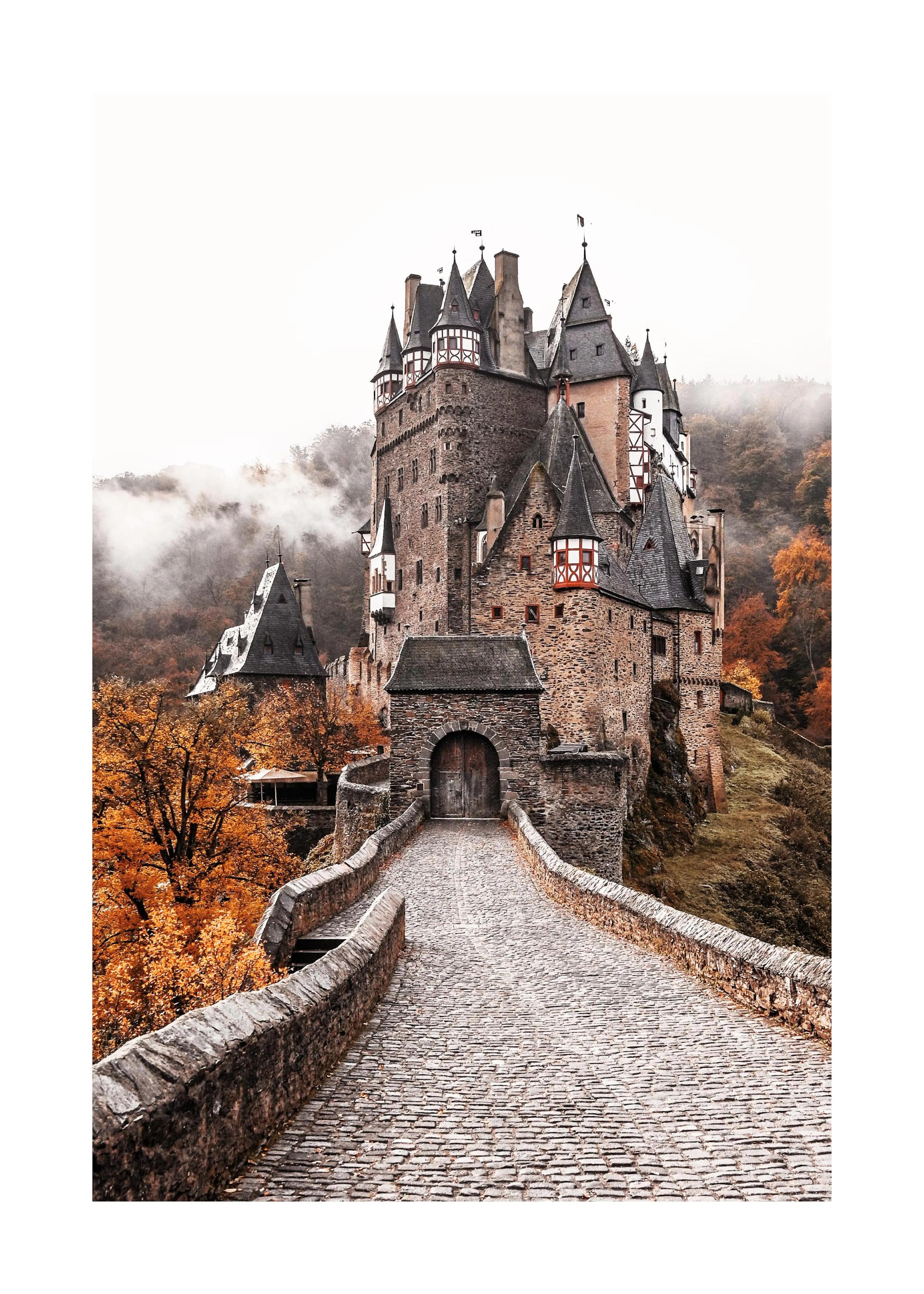 En poster av ett medeltida slott med en stenhällsbro som leder till ingången, omgiven av höstträd och dimma.