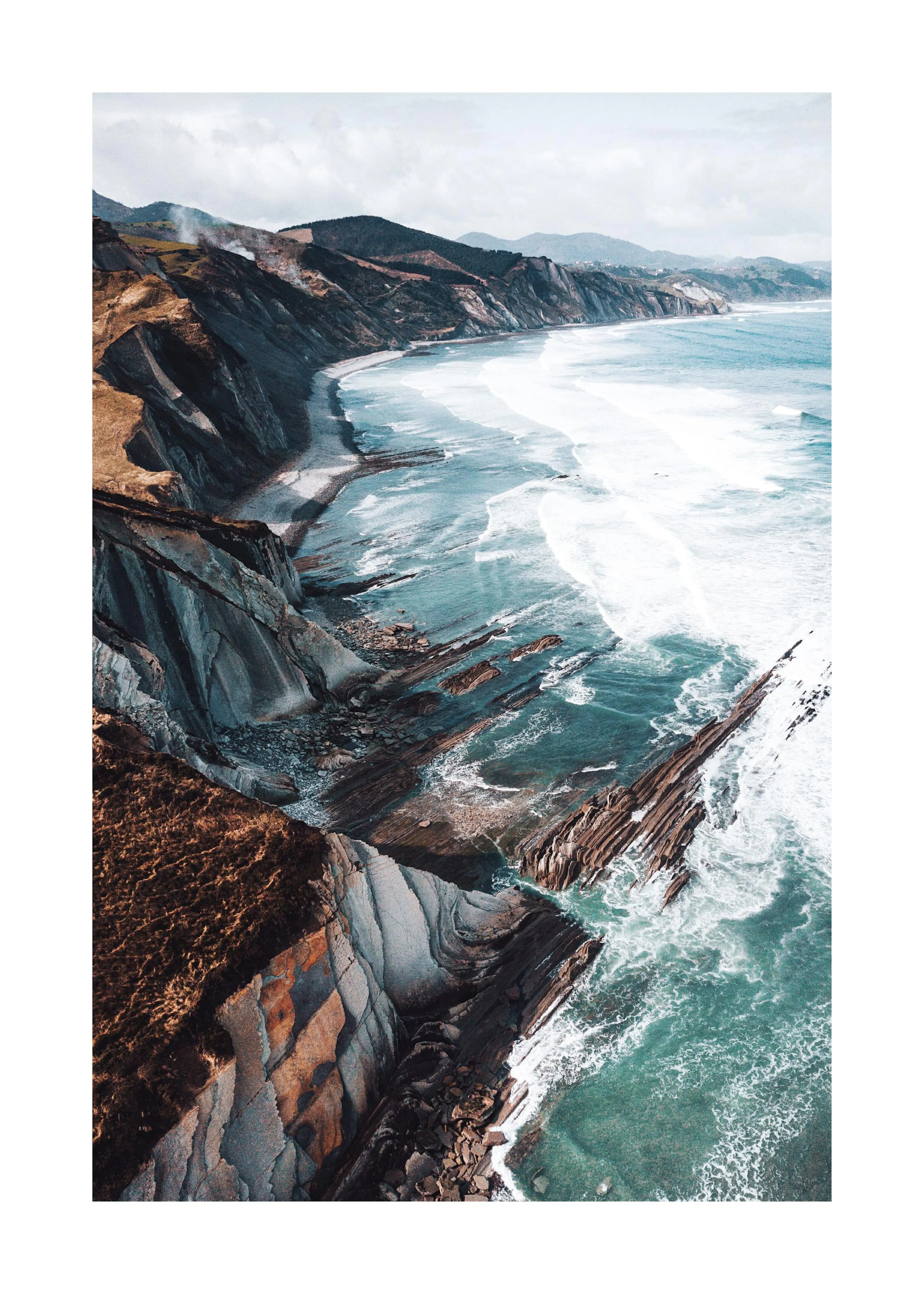Ein Poster einer rauen Küstenlandschaft mit Klippen, die ins Meer ragen, und Wellen, die auf Felsformationen treffen.