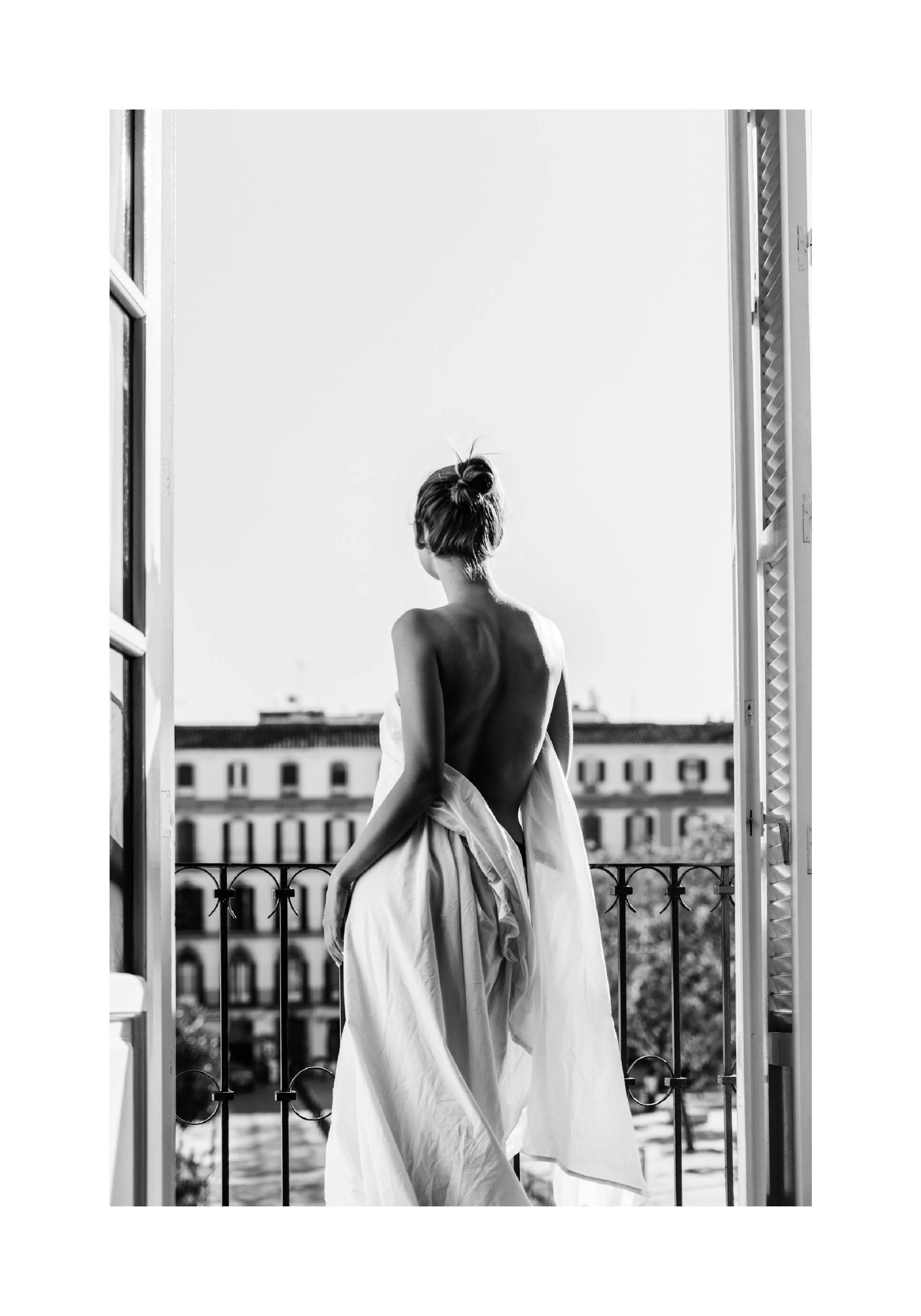 A black and white poster of a woman, seen from behind, wrapped in a sheet, standing on a balcony overlooking a city.