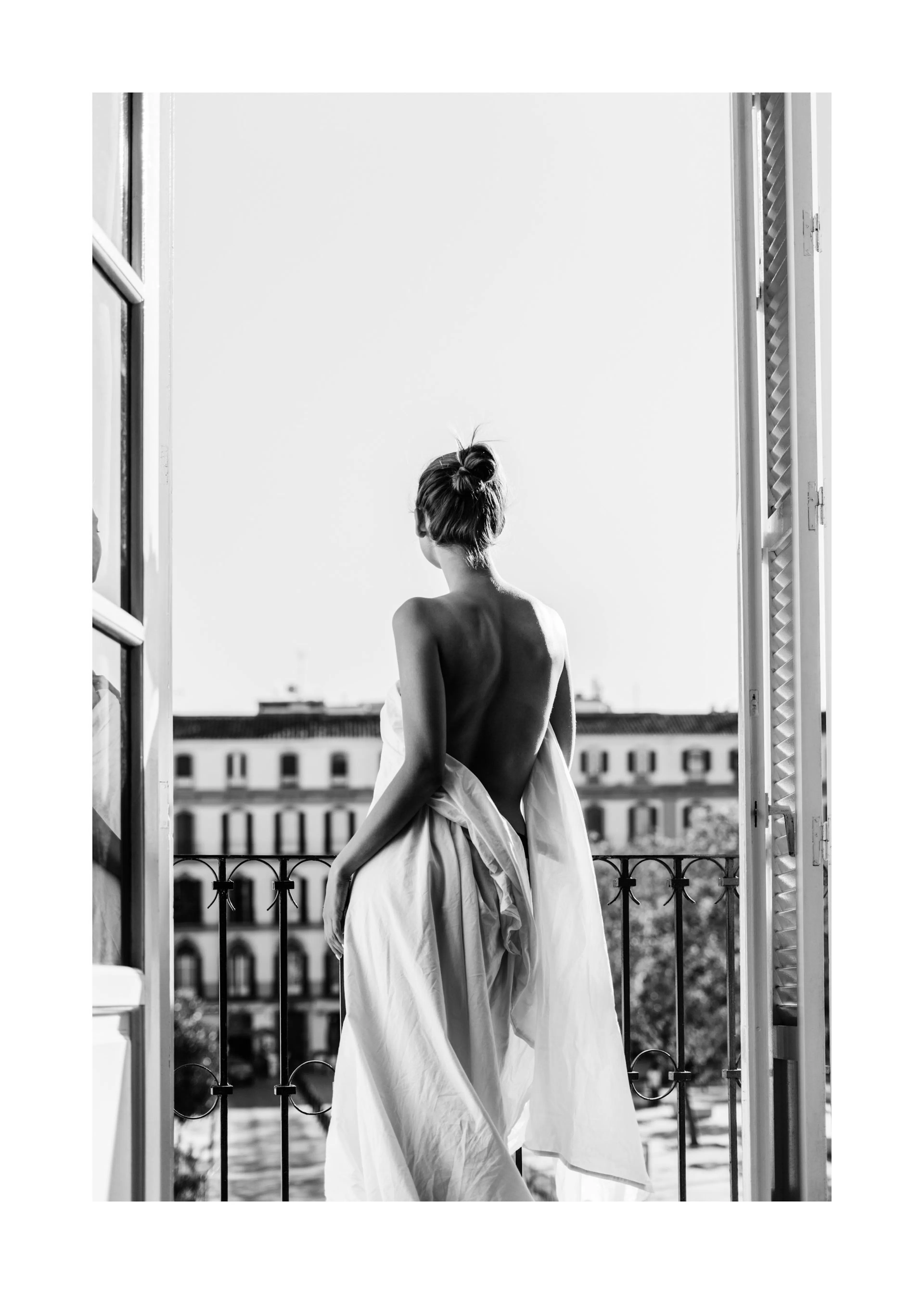 A black and white poster of a woman, seen from behind, wrapped in a sheet, standing on a balcony overlooking a city.