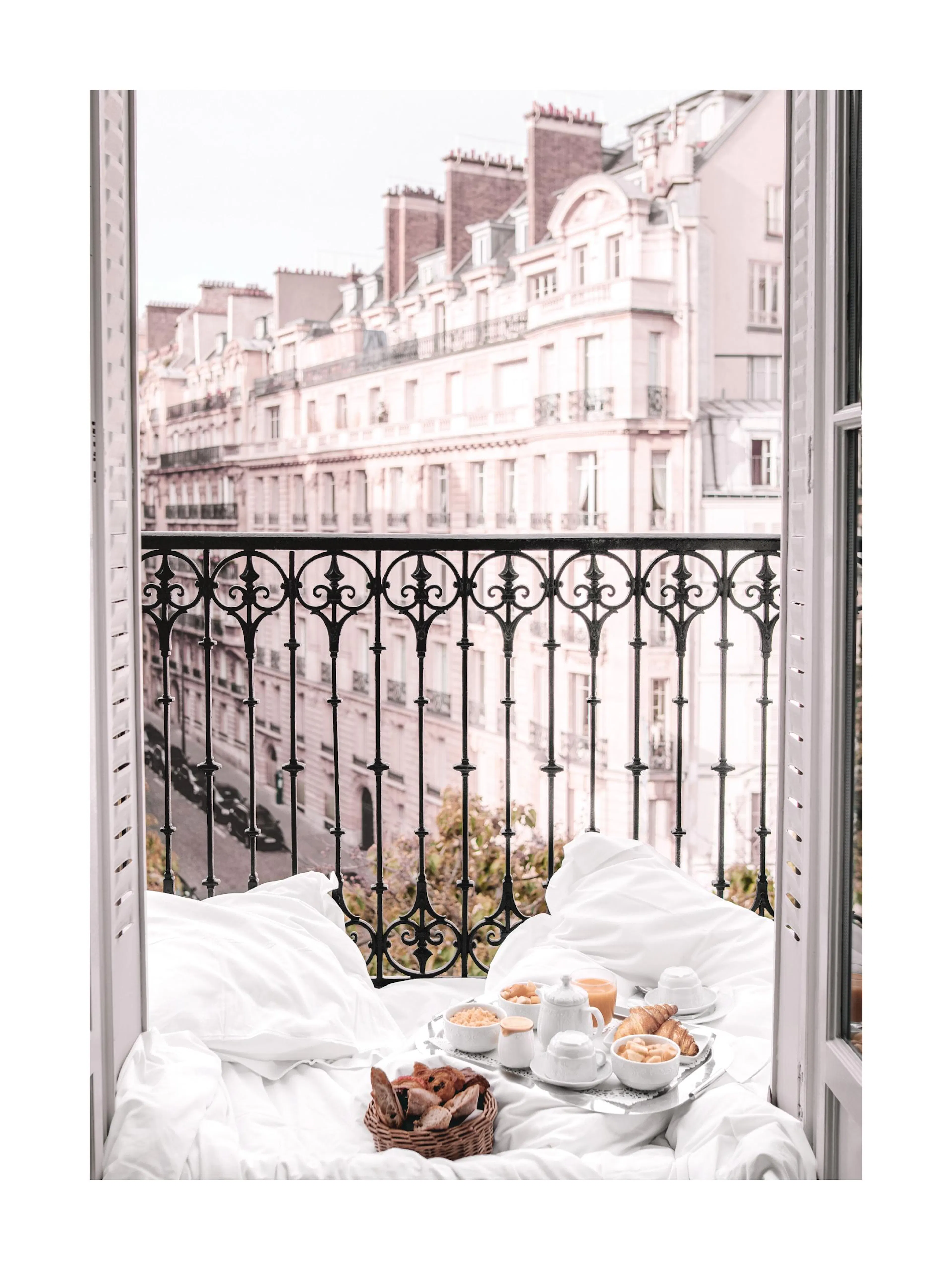 A poster of a balcony view with white sheets, a breakfast tray, and Parisian buildings in the background.