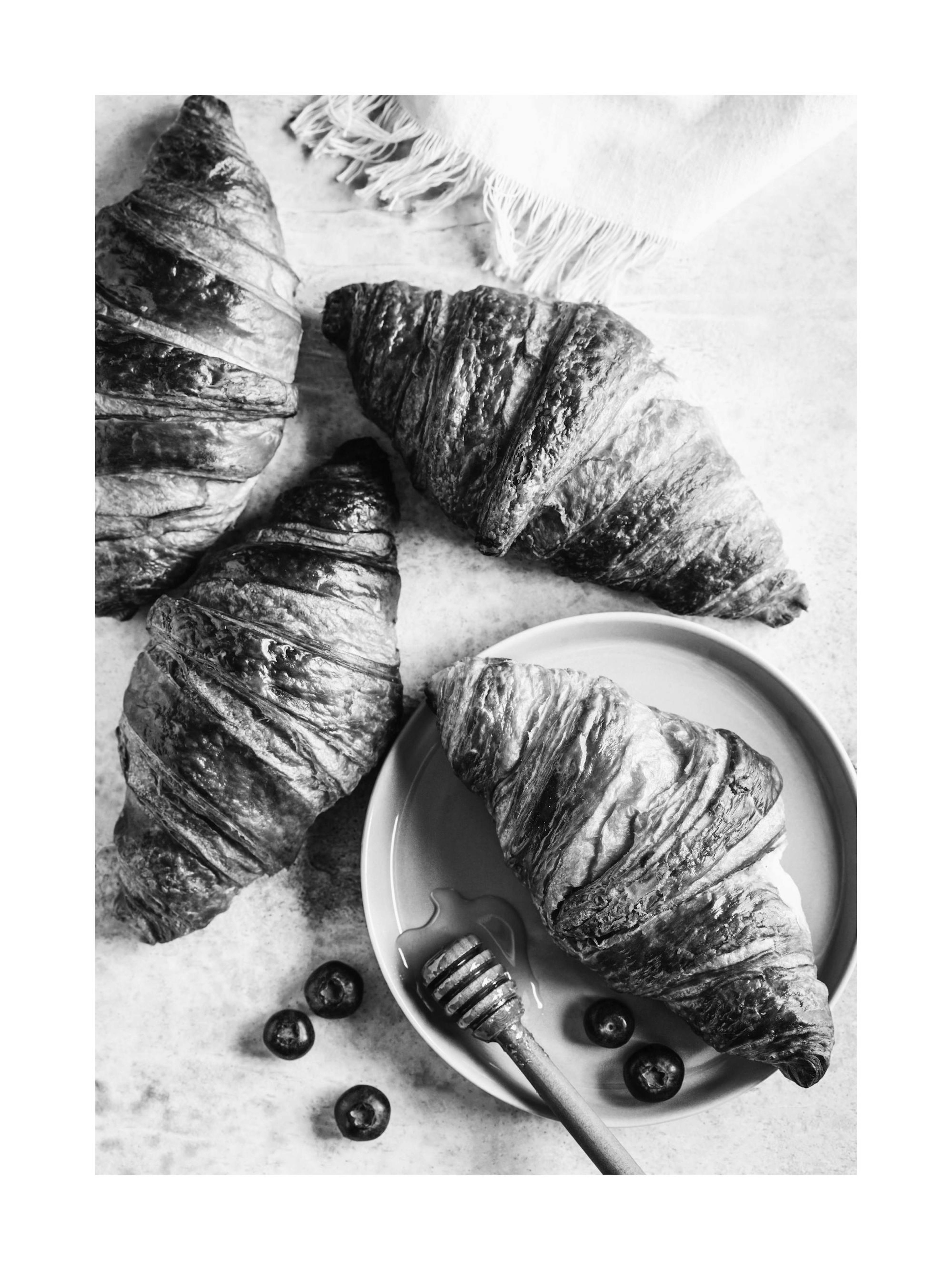En plakat av tre croissanter, en honningdrypper, honning og blåbær i svart-hvitt.