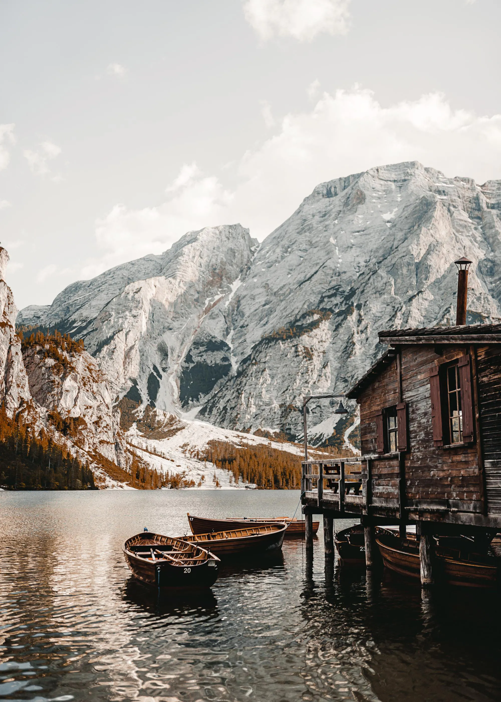 Poster eines Bergsees mit Holzbooten und einer Hütte vor schneebedeckten Alpenbergen.