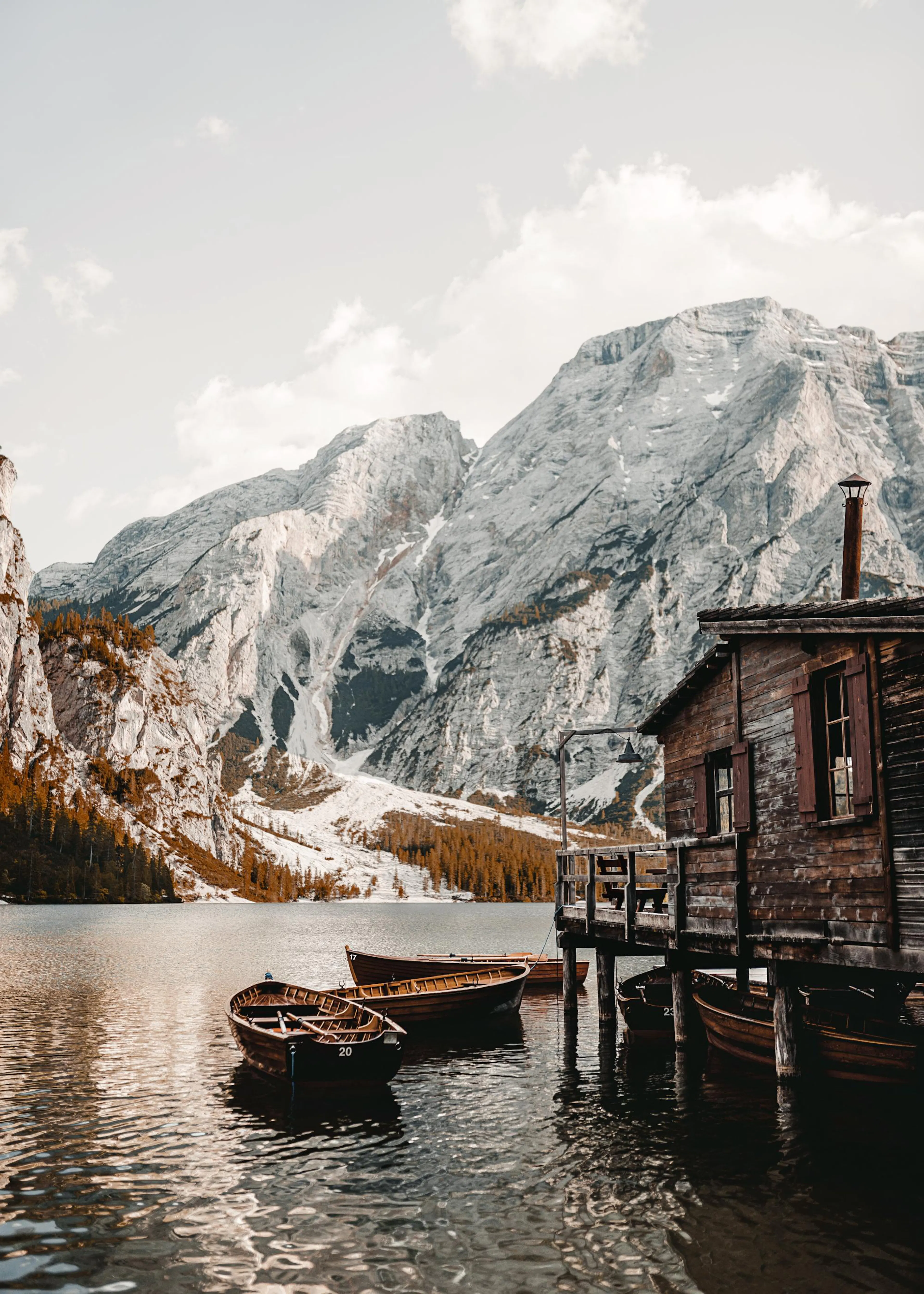 Poster eines Bergsees mit Holzbooten und einer Hütte vor schneebedeckten Alpenbergen.
