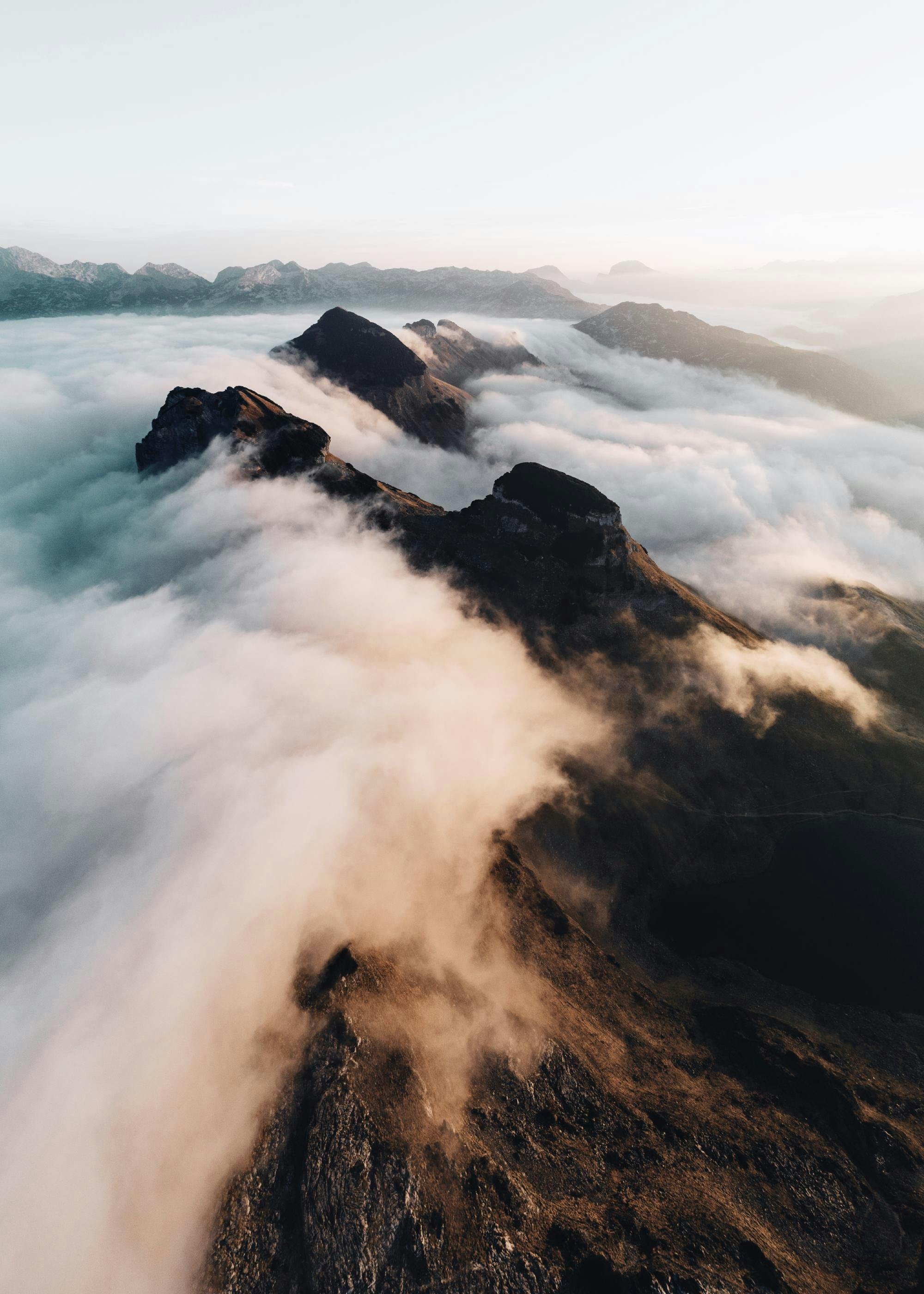 Póster de un paisaje de montaña con picos rocosos asomando entre nubes bajas al amanecer.
