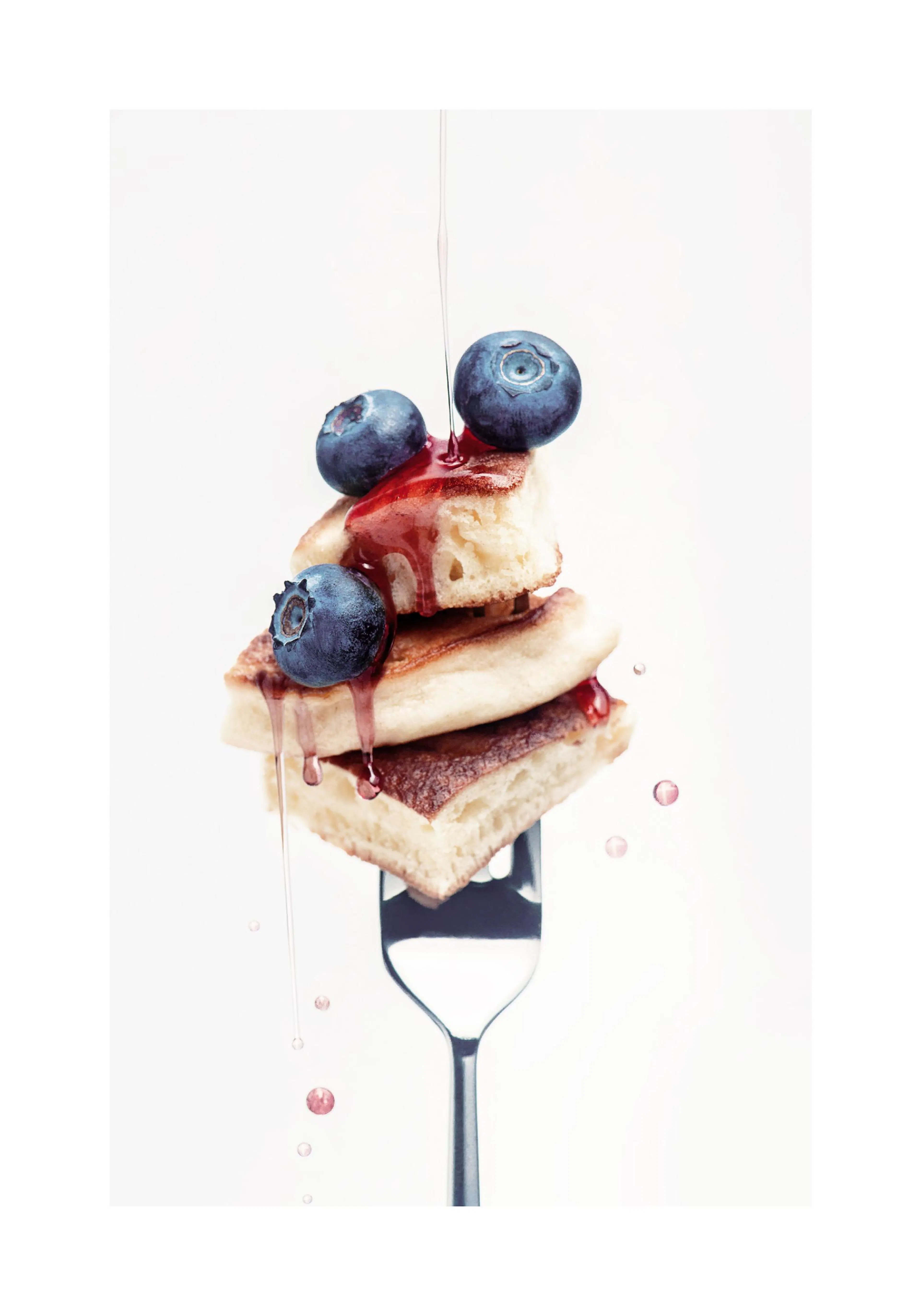 A poster featuring a stack of mini pancakes and blueberries on a fork, with red syrup drizzling down.
