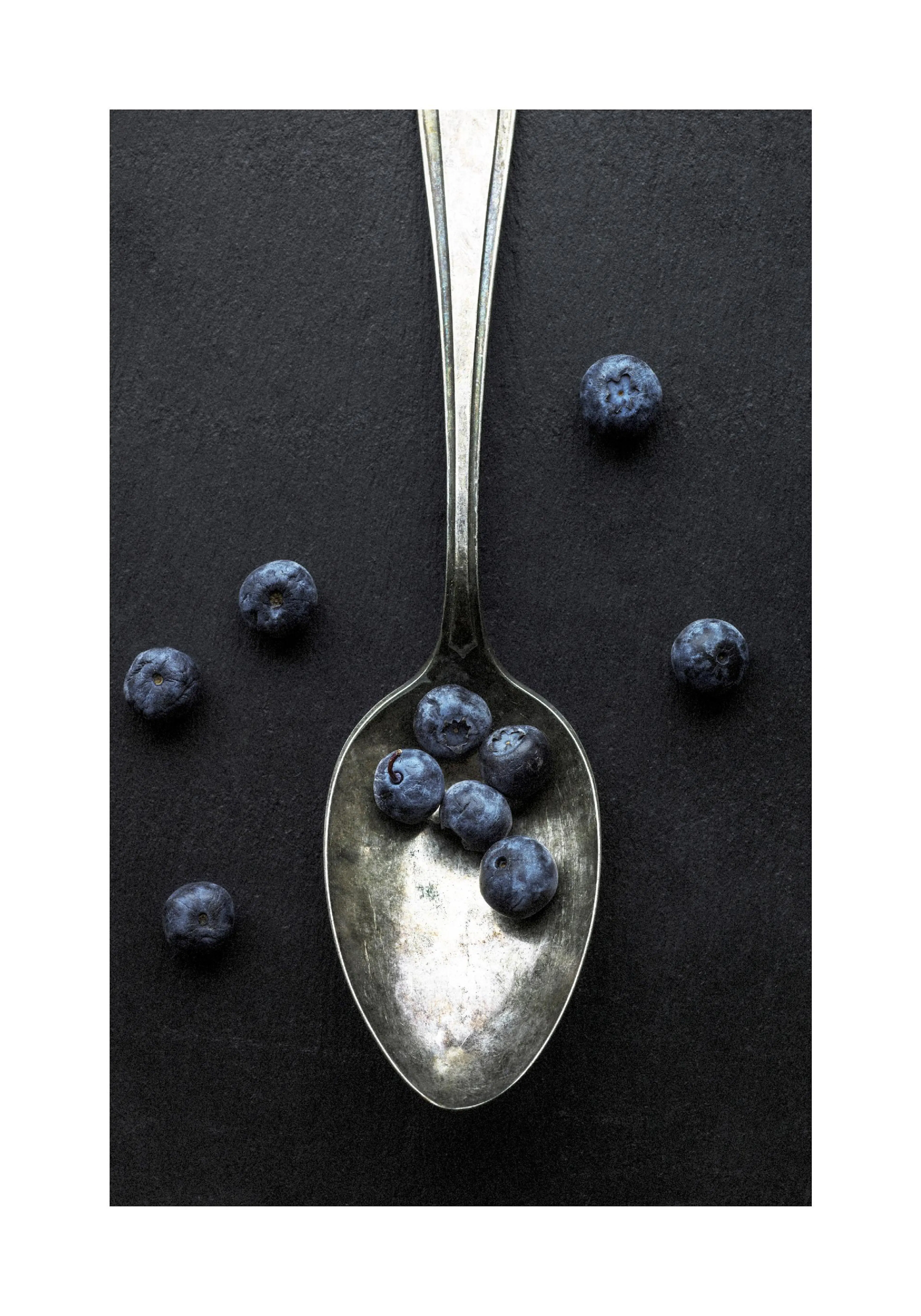 黒い背景に銀色のスプーンと散らばる複数のブルーベリーが写ったポスター。