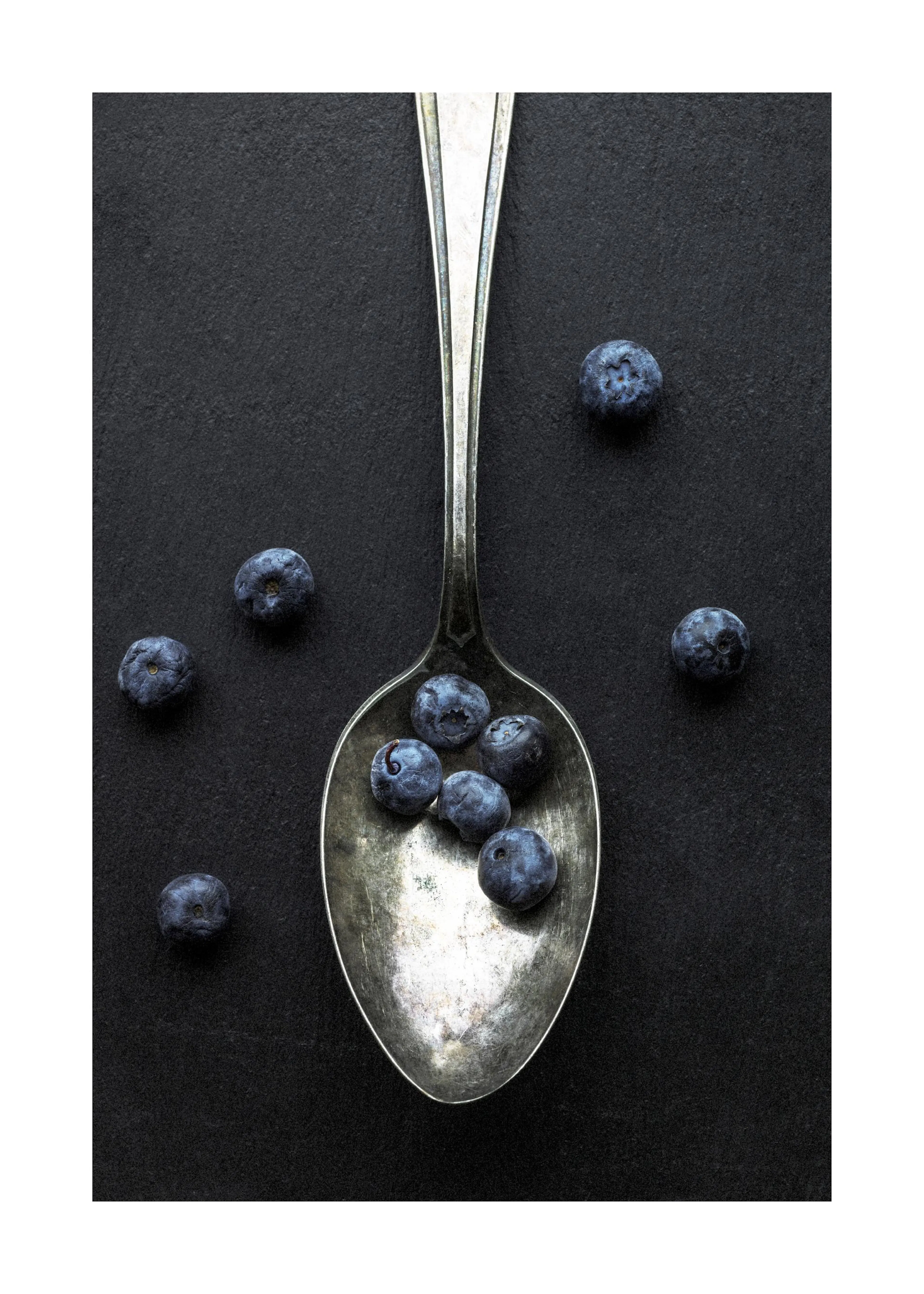 Poster dune cuillère en argent avec des myrtilles sur un fond noir texturé, vue de dessus.