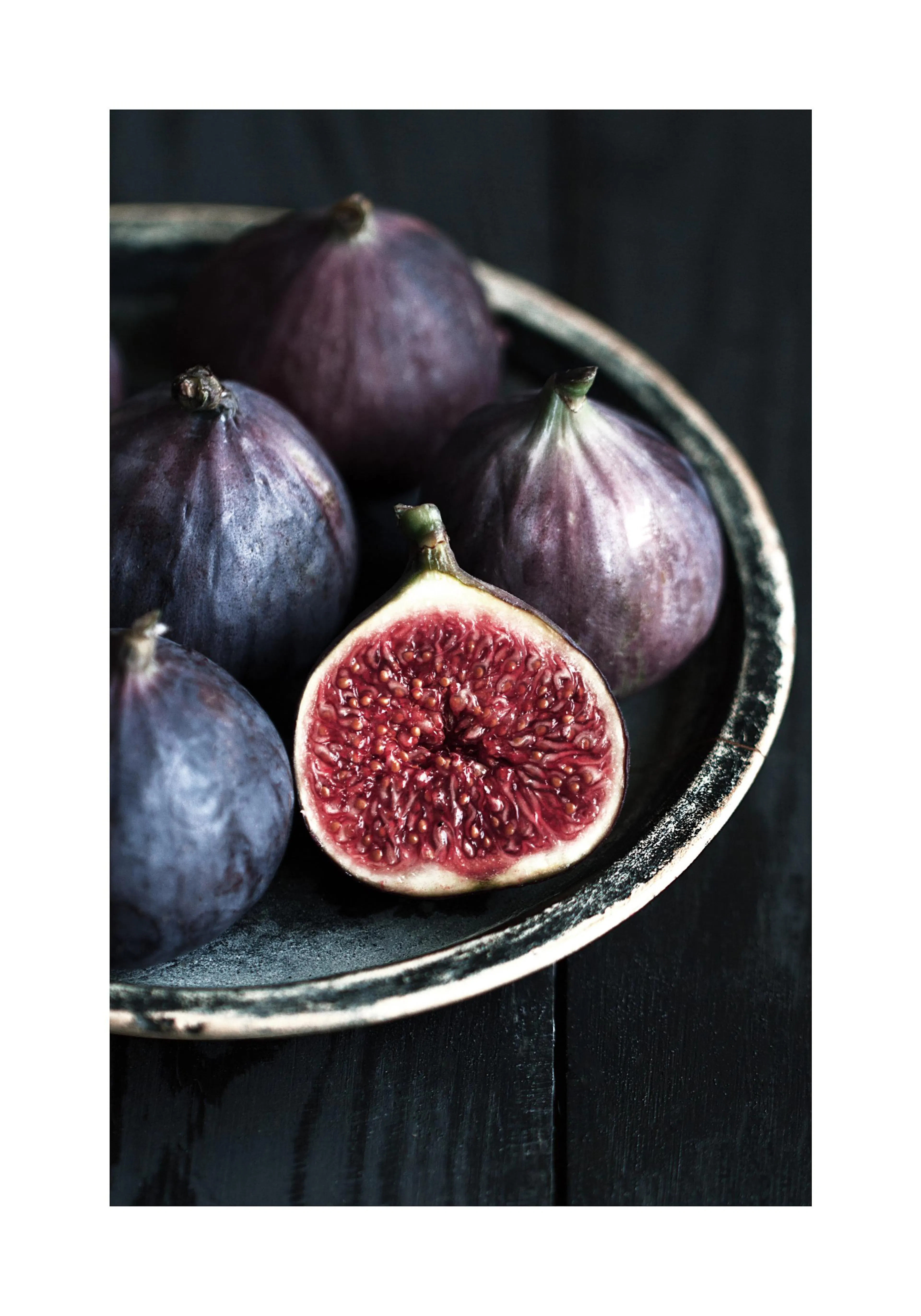A poster featuring a close-up of dark purple figs on a rustic plate, with one fig cut open to reveal its red interior.