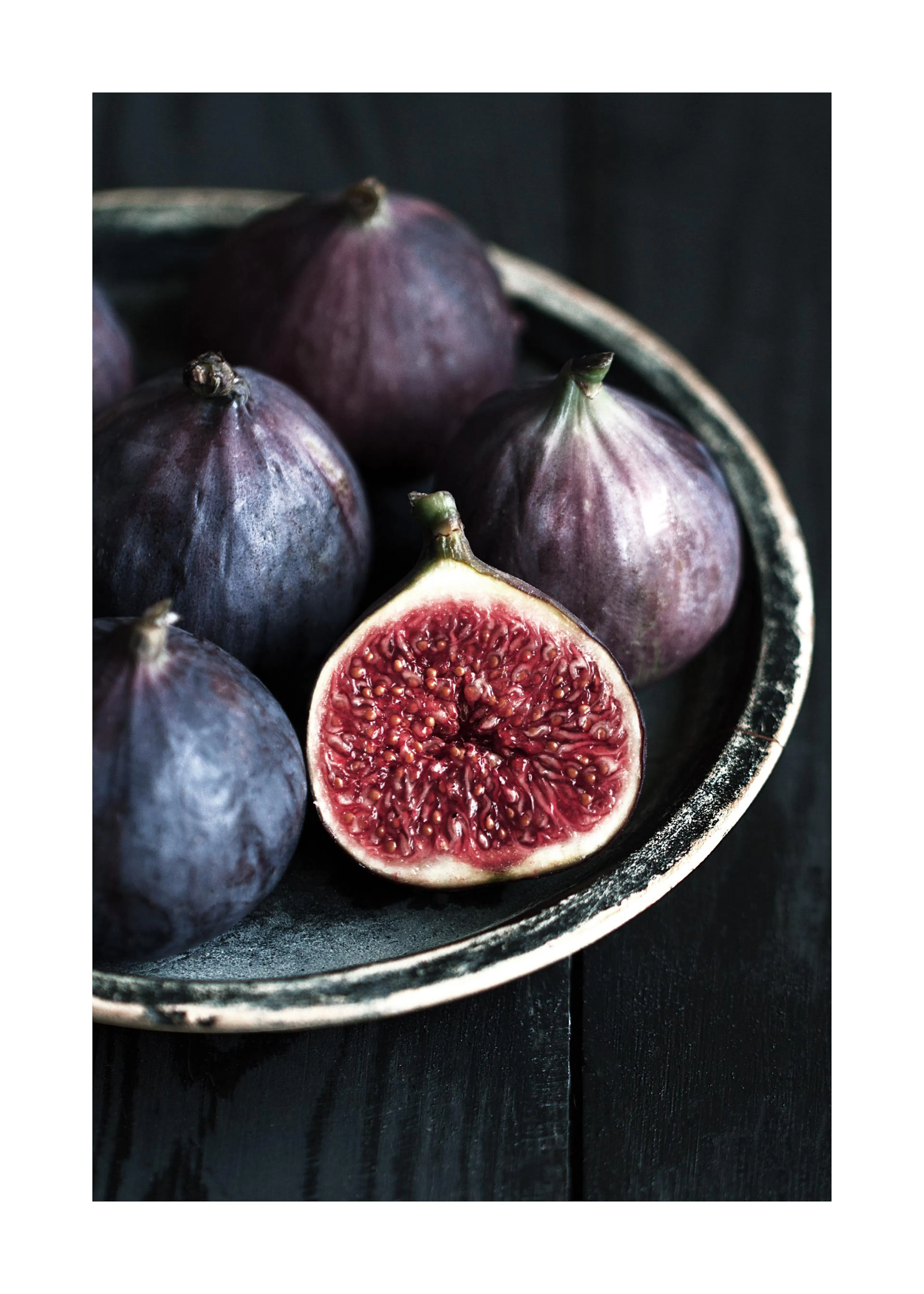 A poster featuring a close-up of several dark purple figs, with one cut in half revealing its vibrant red interior, all on a dar