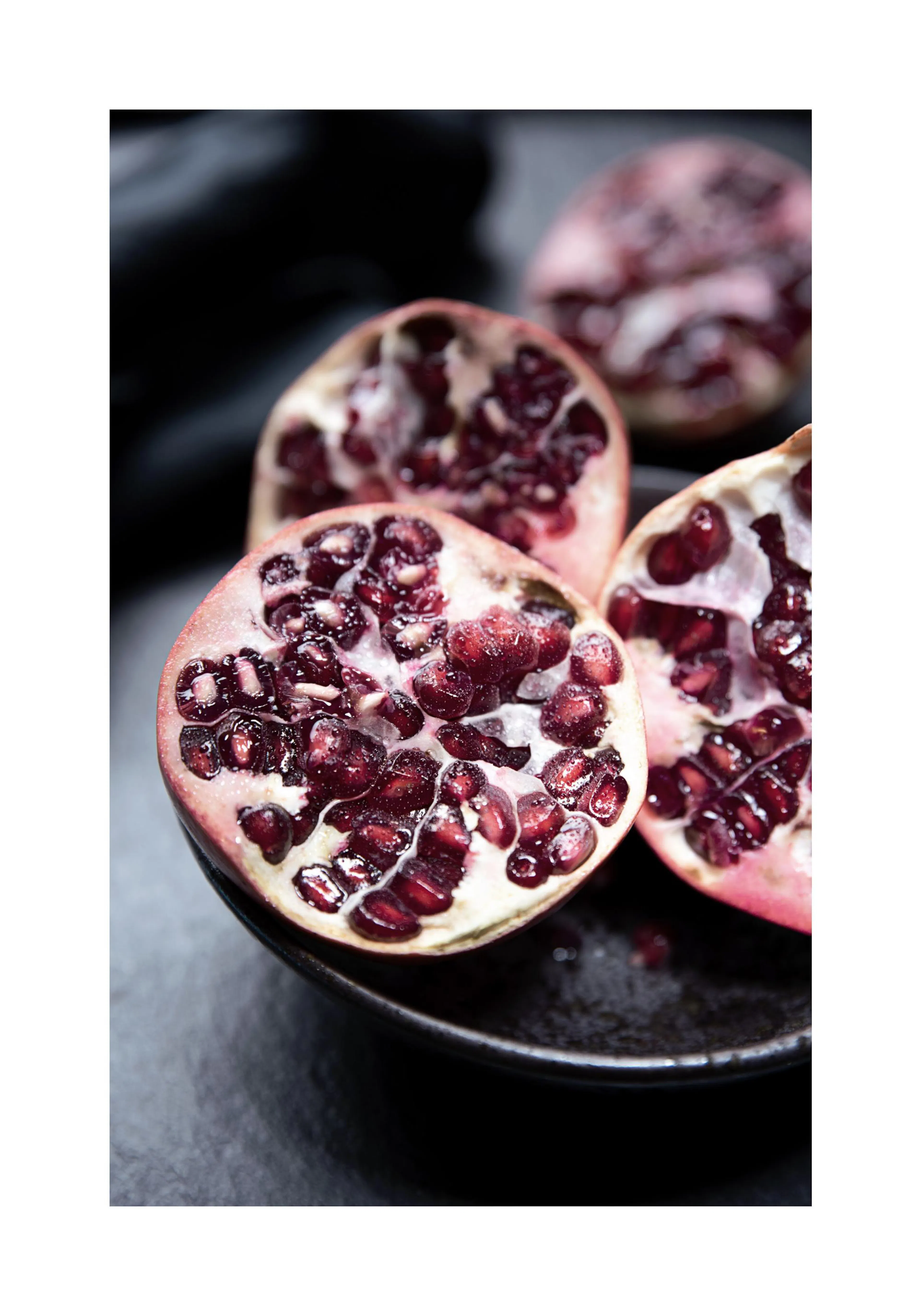 A poster featuring three vibrant red pomegranates, cut open to reveal their juicy arils, on a dark background.