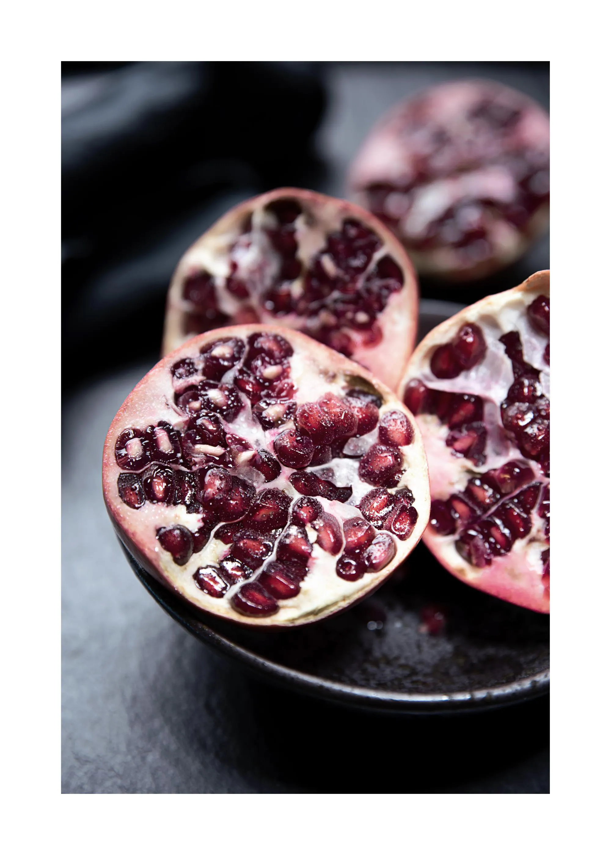A close-up poster of three open pomegranates with vibrant red seeds on a dark background.