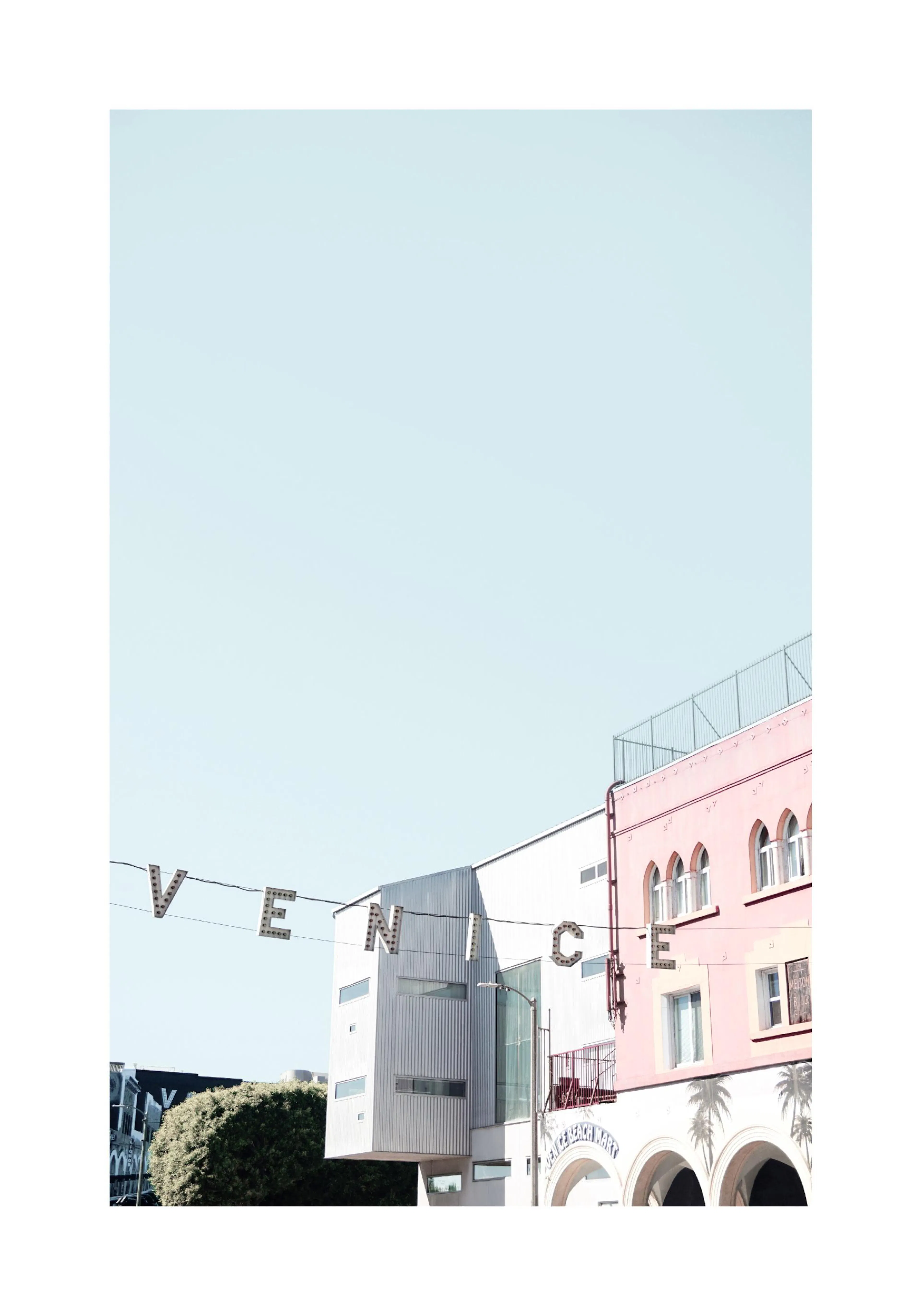 A poster featuring a light blue sky above a pink building with arches and a white building, with VENICE signs hanging.