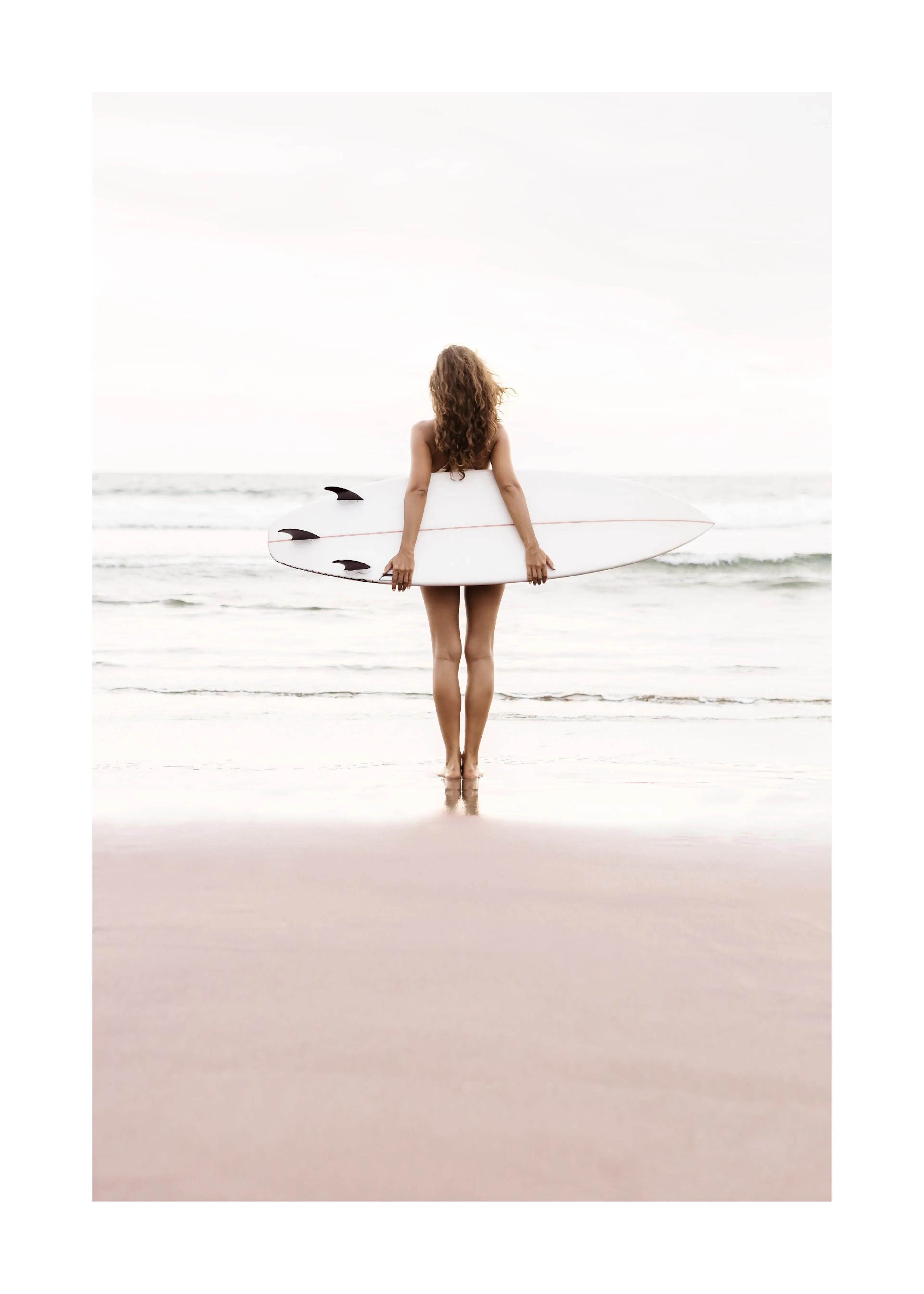 Poster: Frau mit Surfbrett steht am Strand und blickt auf das Meer.