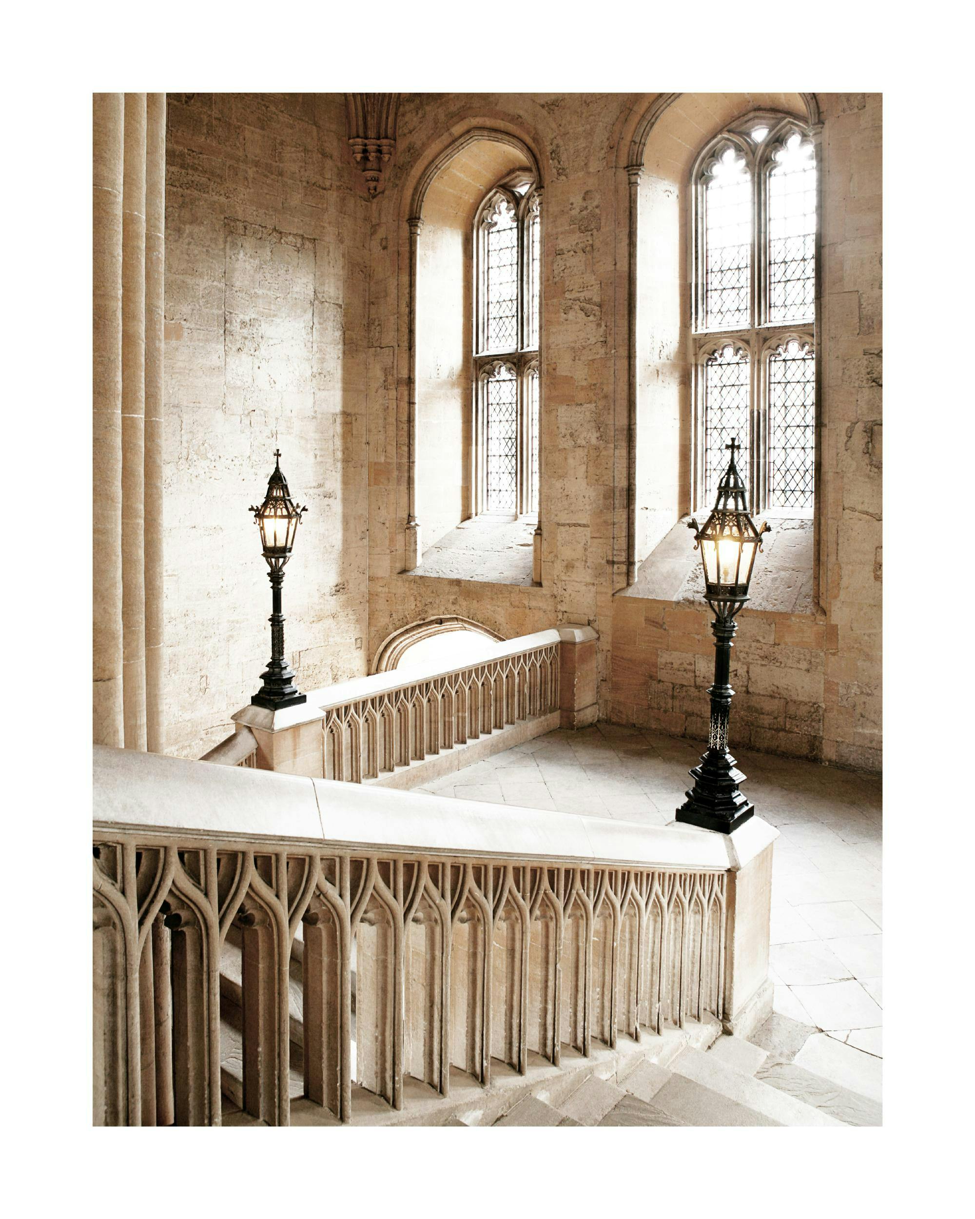 A poster featuring a grand stone staircase with ornate railings and two illuminated lamps in a historic building.