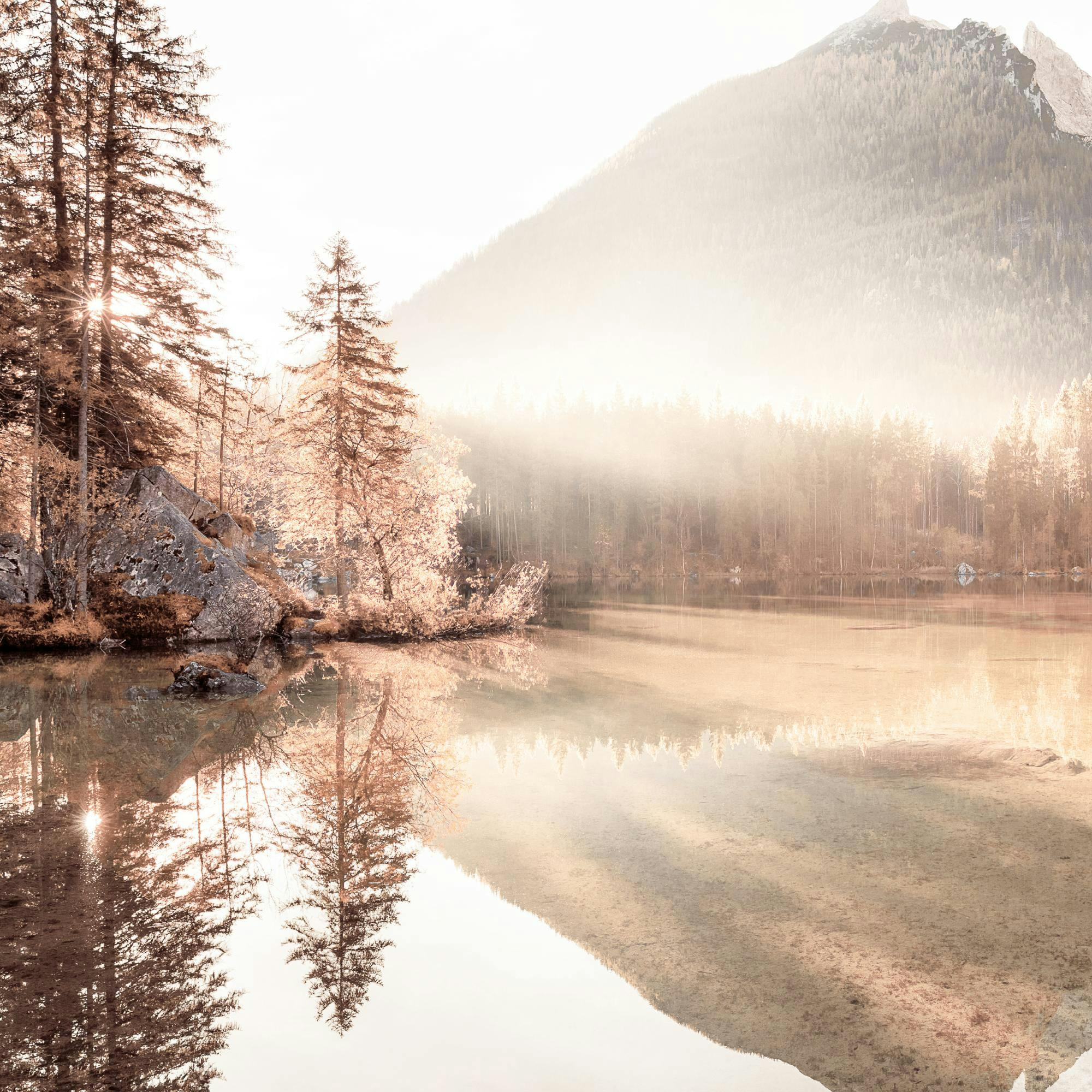 Ruskeasävyinen juliste, jossa järvi heijastaa vuoria ja metsää auringonnousun aikaan. Vesi peilaa valoa ja puita.