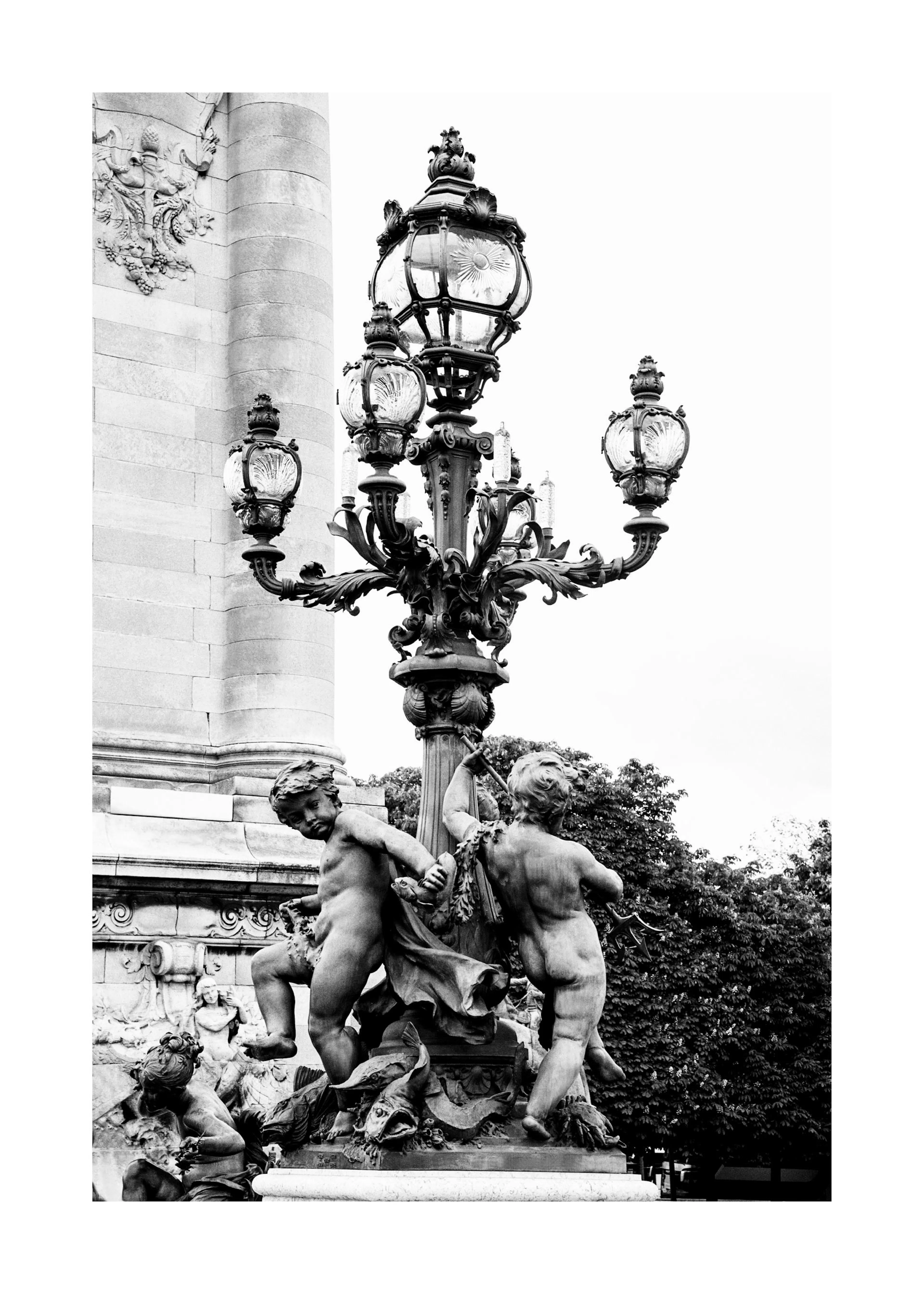 Poster alb-negru cu statui de îngeri sculptați și un stâlp de iluminat ornamentat, pe fundalul unui copac.