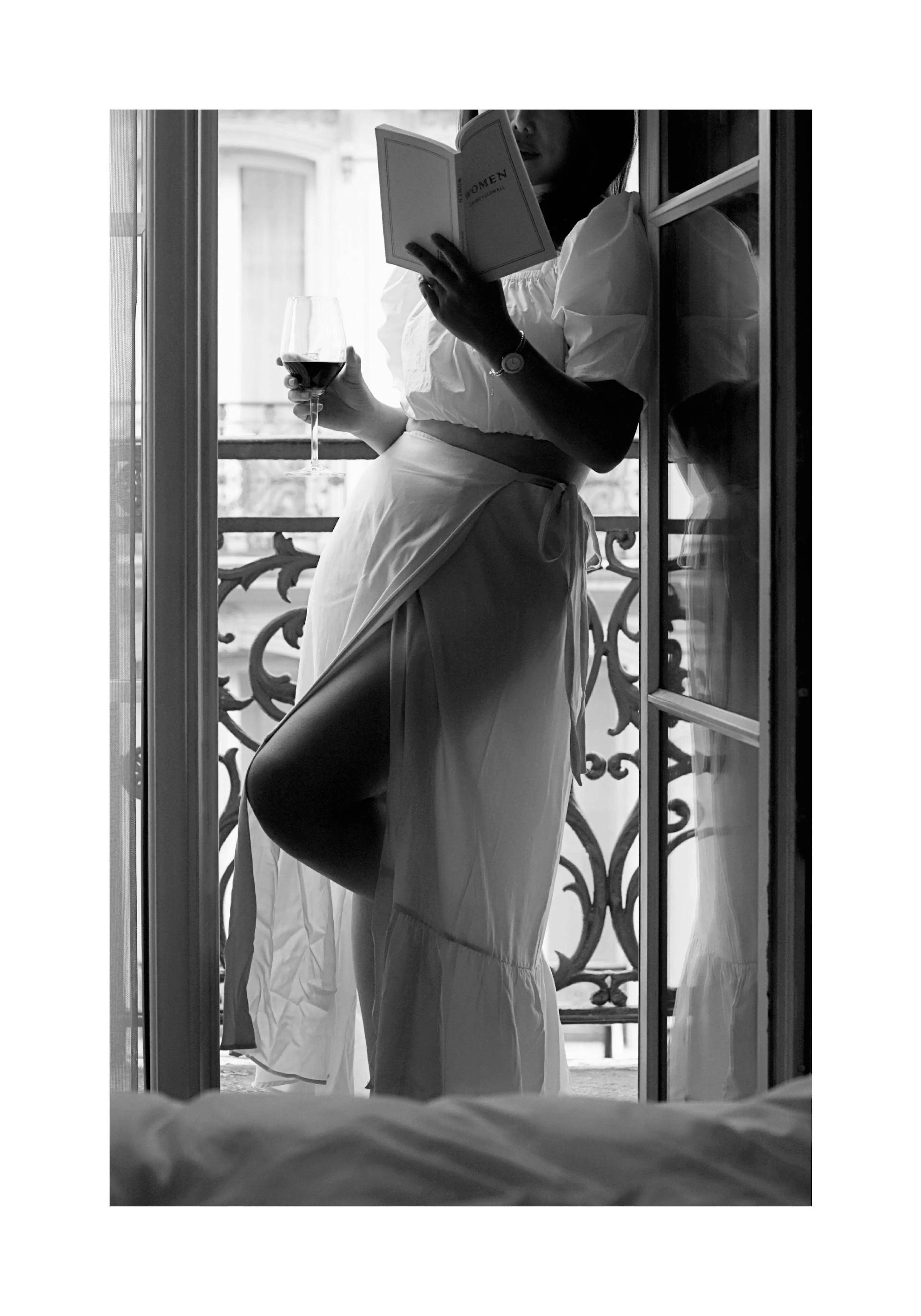 Un poster en noir et blanc dune femme lisant un livre et tenant un verre de vin sur un balcon.