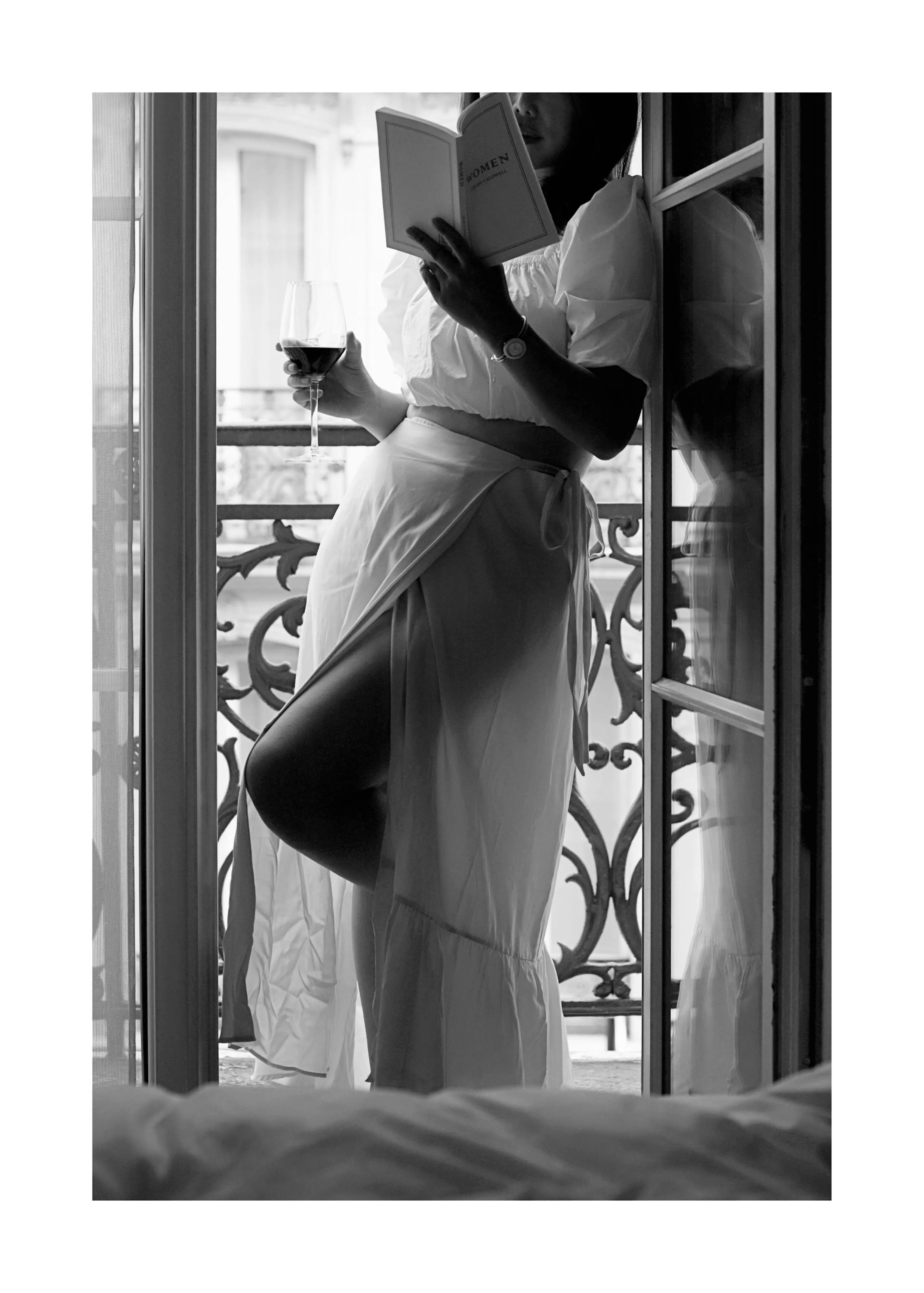 Un poster en noir et blanc dune femme lisant un livre et tenant un verre de vin sur un balcon.